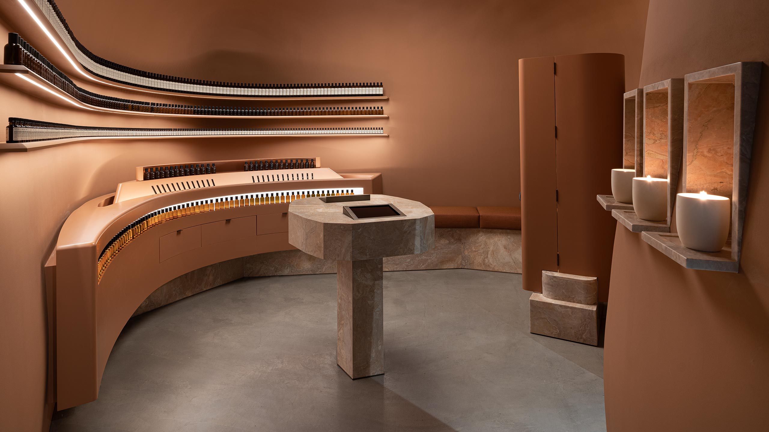 Three Aesop candles burning on a rose coloured shelf on a wall