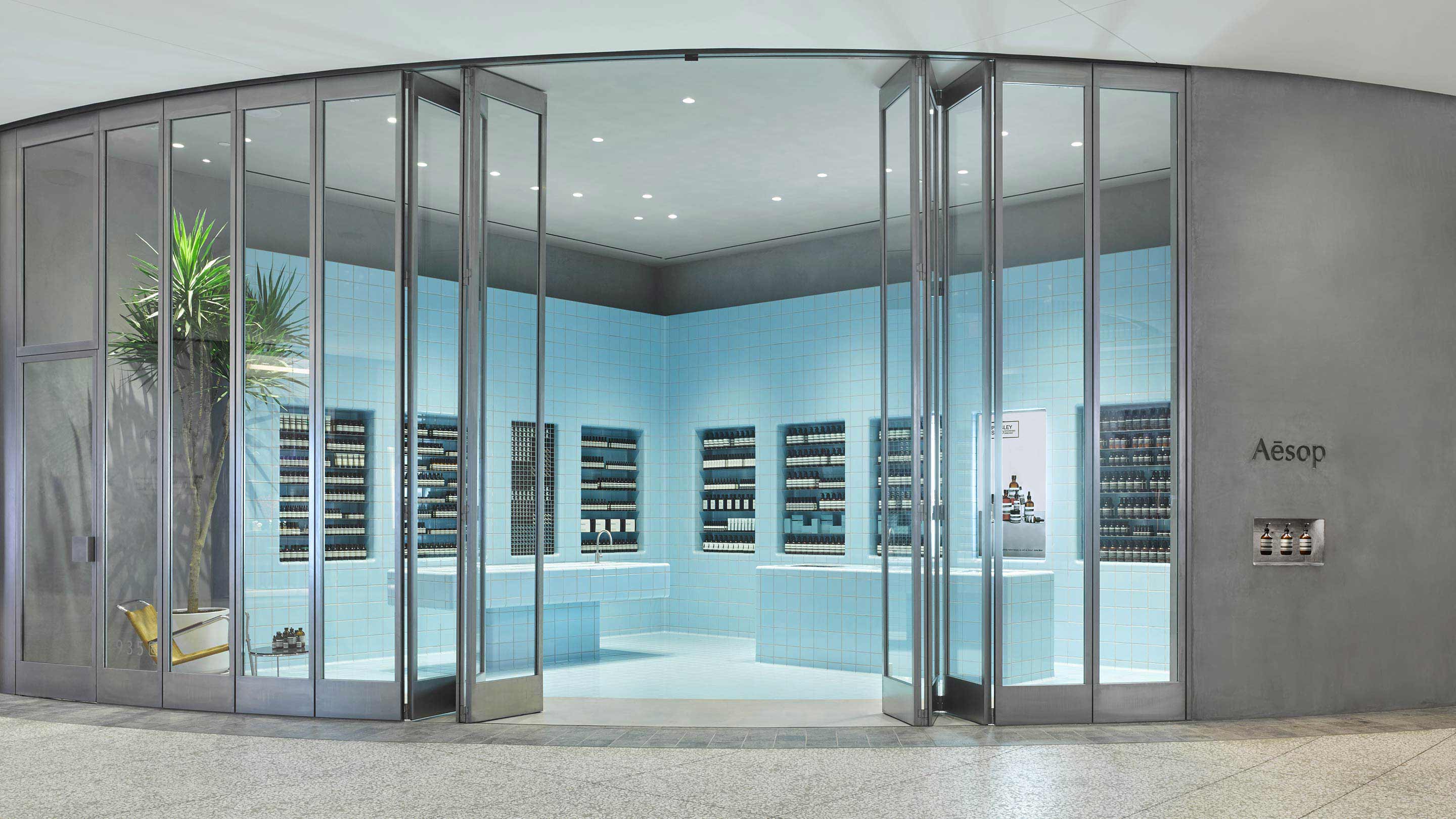 Sliding glass doors with steel frames open displaying the light-blue tiled store interior. 