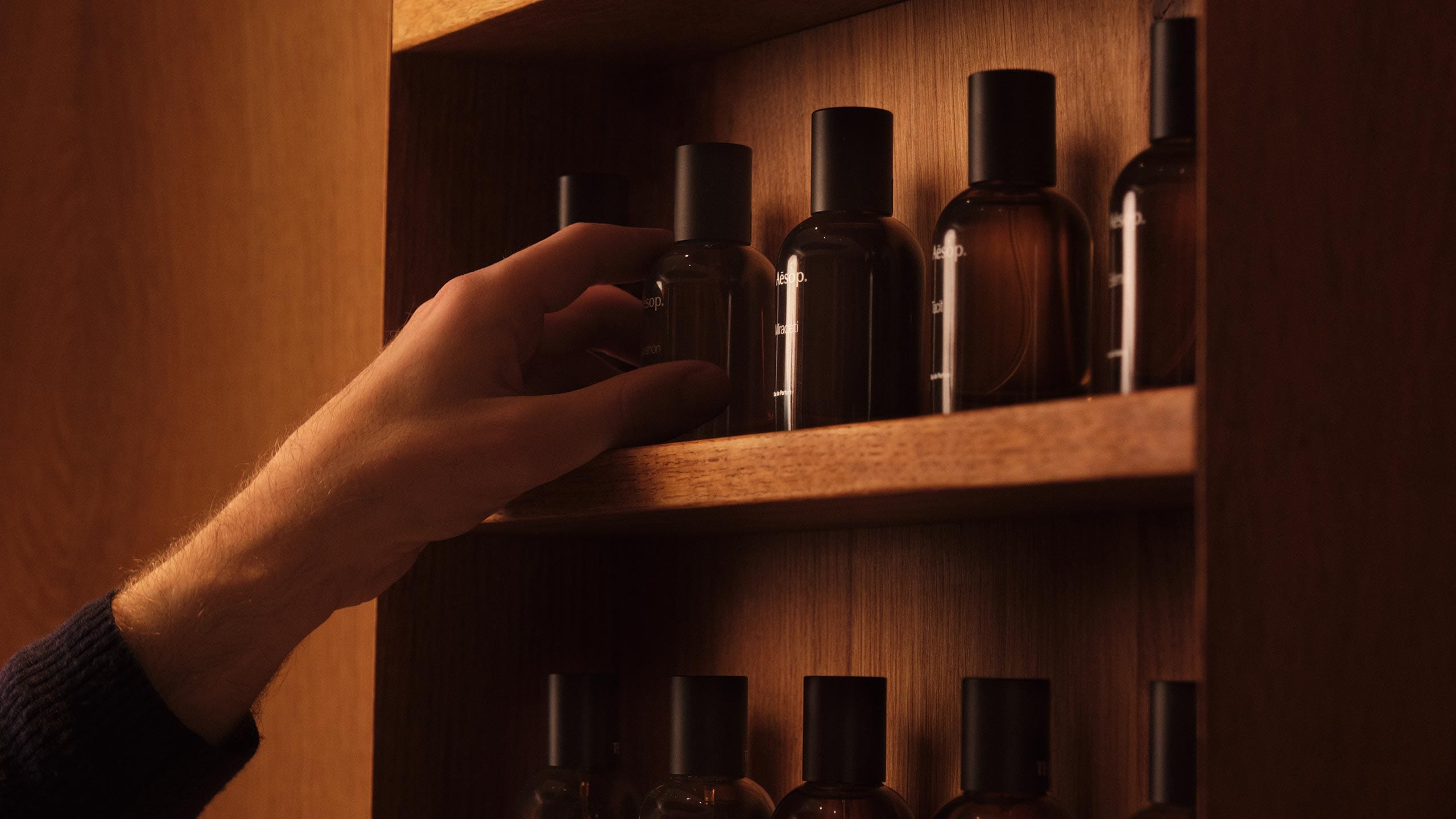A hand reaching out to grab the Aesop fragrance from the wooden shelves