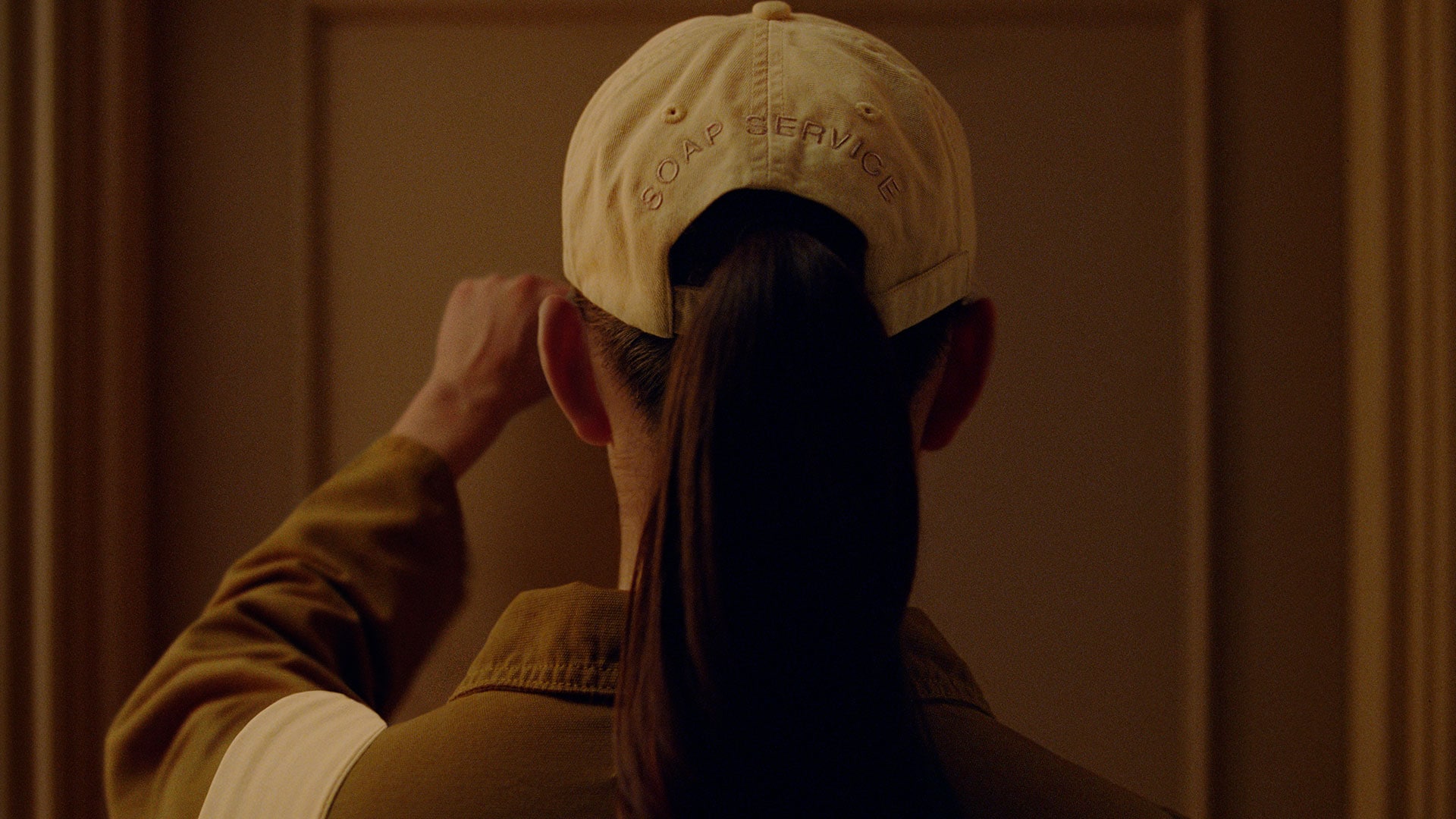 Rear view of someone knocking on a door wearing a white hat with ‘SOAP SERVICE’ embroidered on the back.