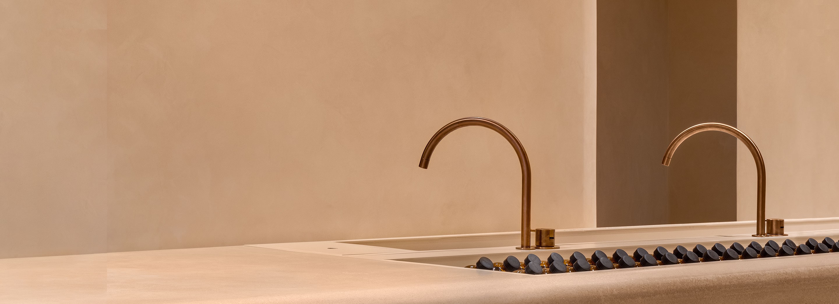 A brass sink against a peach-coloured wall with Aesop product laid out.