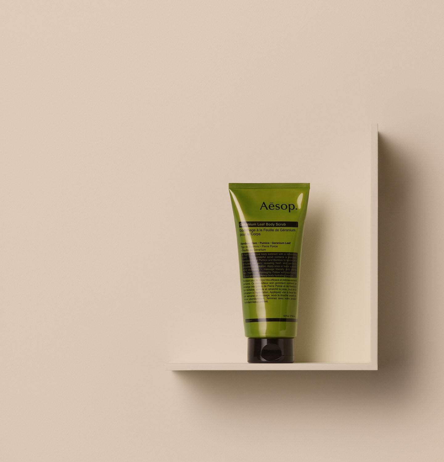 Aesop geranium leaf body scrub in green tube placed on a beige wall