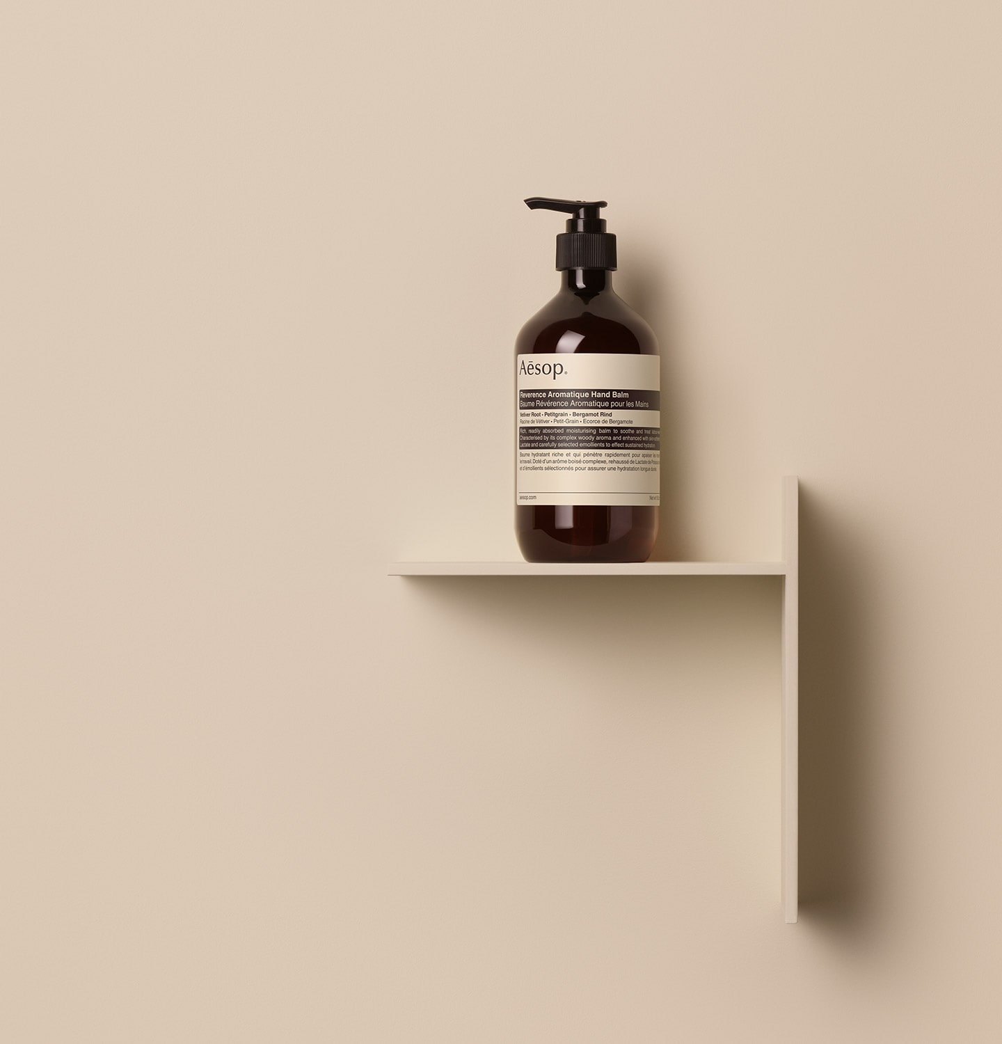 Aesop reverence aromatique hand balm in amber bottle with pump placed on a beige wall