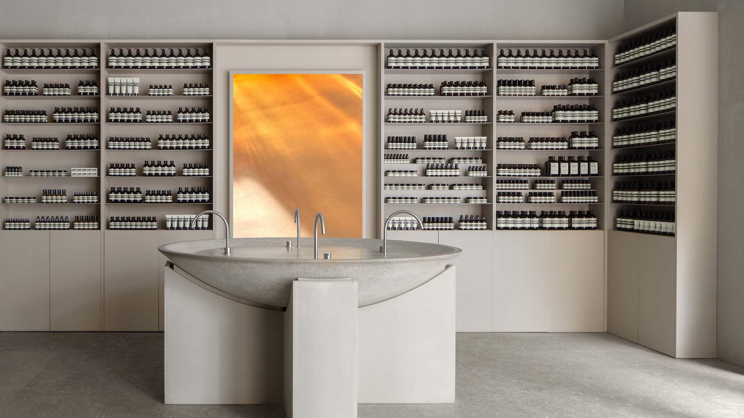 Aesop Eaton Toronto Store circular basin and visual display behind this, Aesop product displays flank the basin