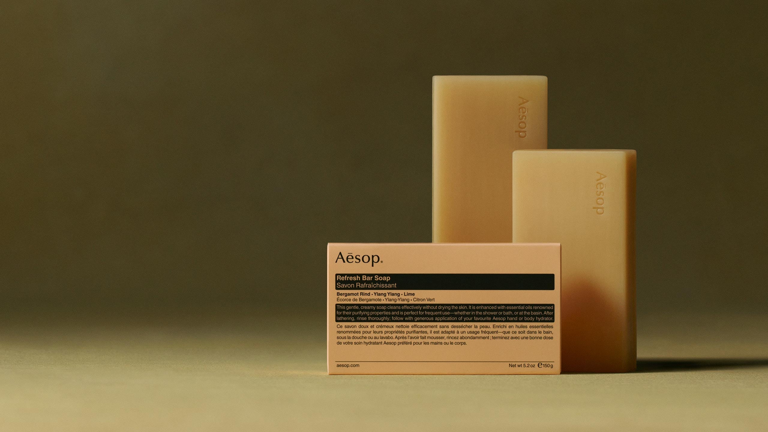 Aesop Refresh bar soaps placed horizontally behind the packaging in textured dark green background