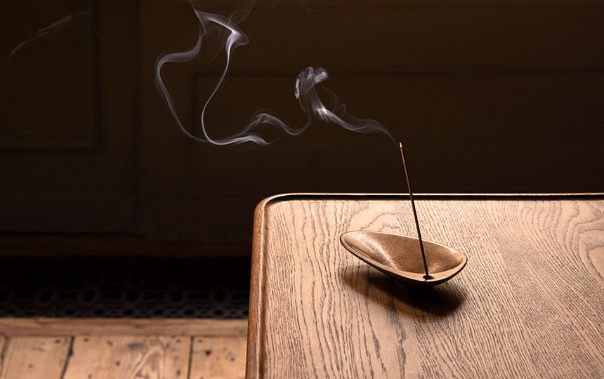 Aesop bronze incense holder with burning incense on top of a wooden table