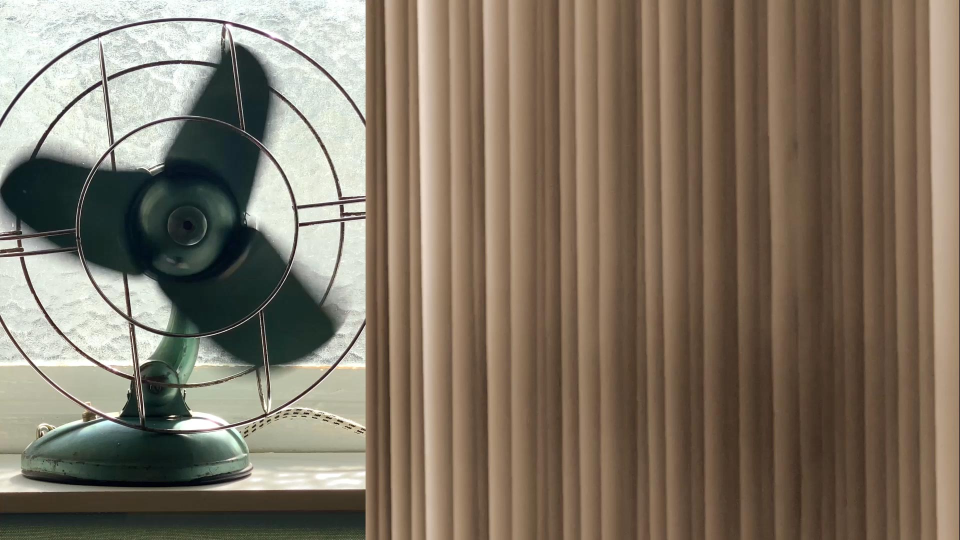 Moving image of old-fashioned table fan spinning and vertical blinds moving with breeze.