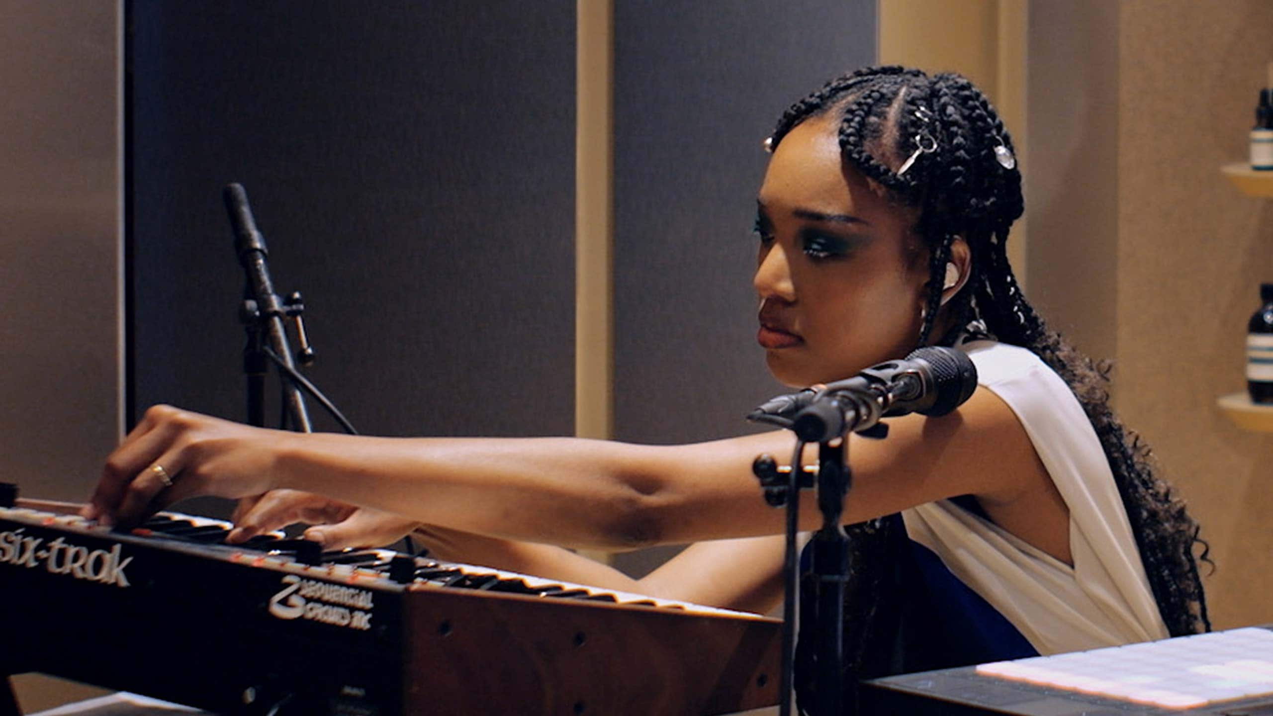 Kiala Ogawa operating a synthesizer surrounded by amber glass bottles in an Aesop store.