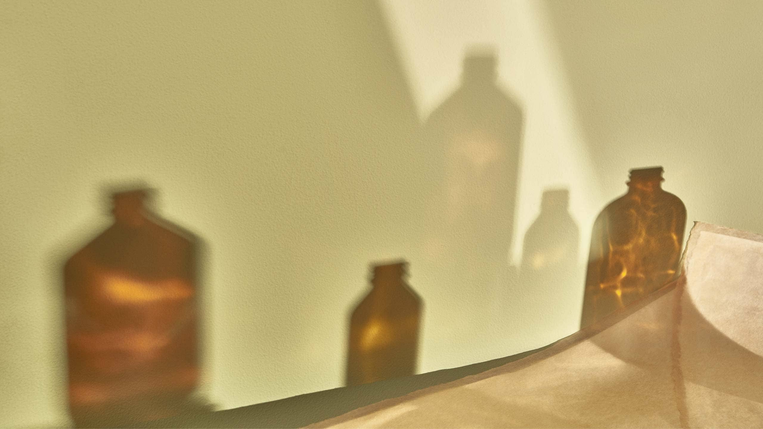 Brown glass bottles with ray of light reflecting silhouettes on a wall.