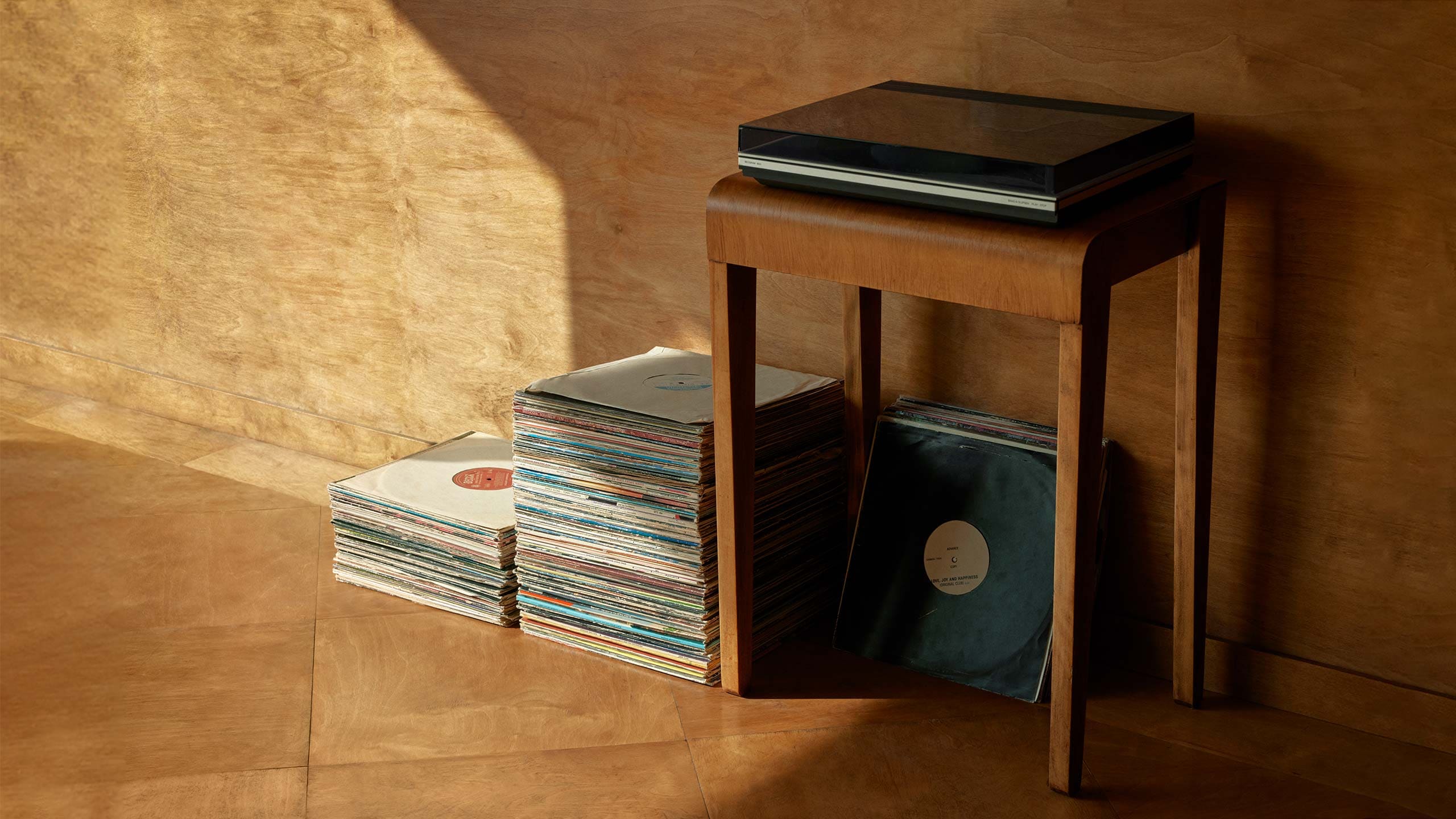 A turntable on a mid-century wooden table with a stack of vinyl records resting alongside it.