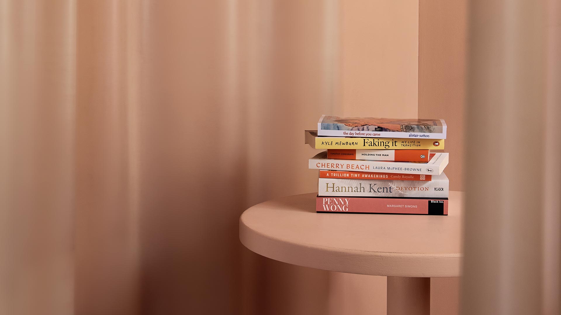 A stack of books sitting on top of a pink stool surrounded by soft-pink curtains.