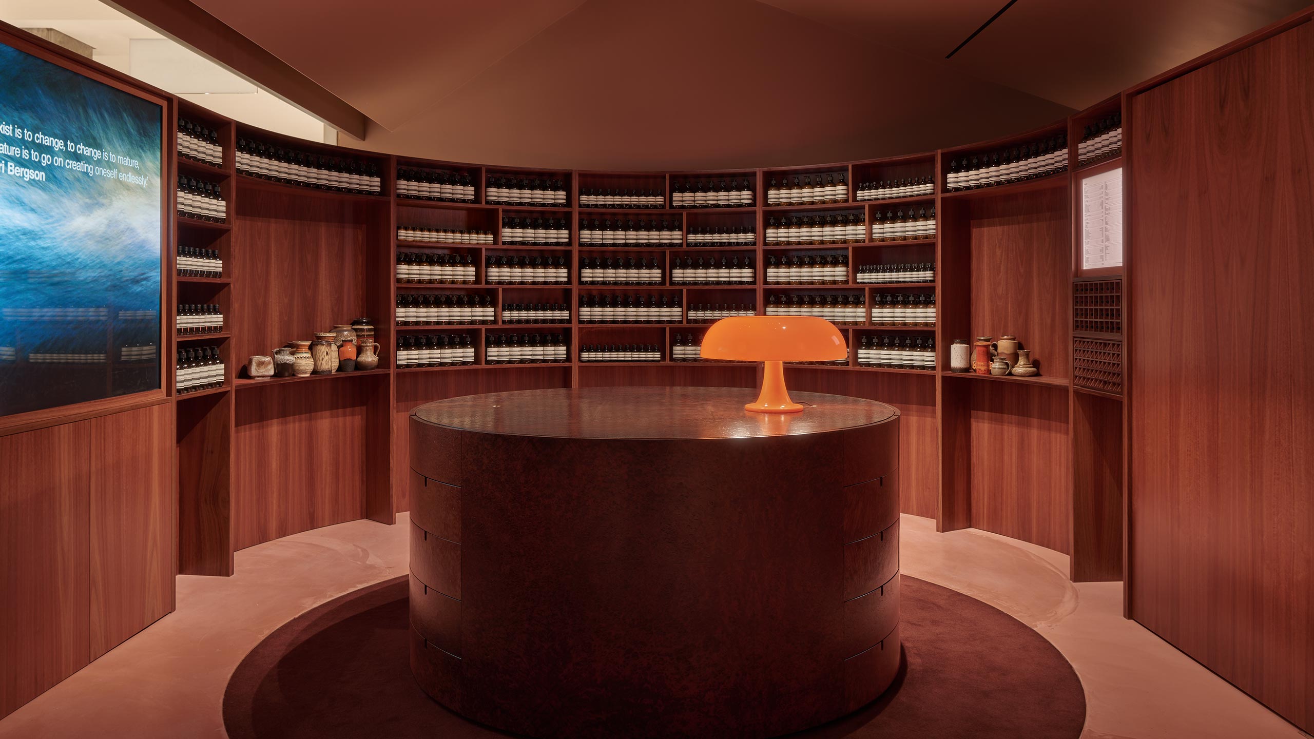 Round walls surround the customer service desk, crafted out of rich, dark wood and a marble top. A twentieth-century style mushroom lamp sits atop the counter.