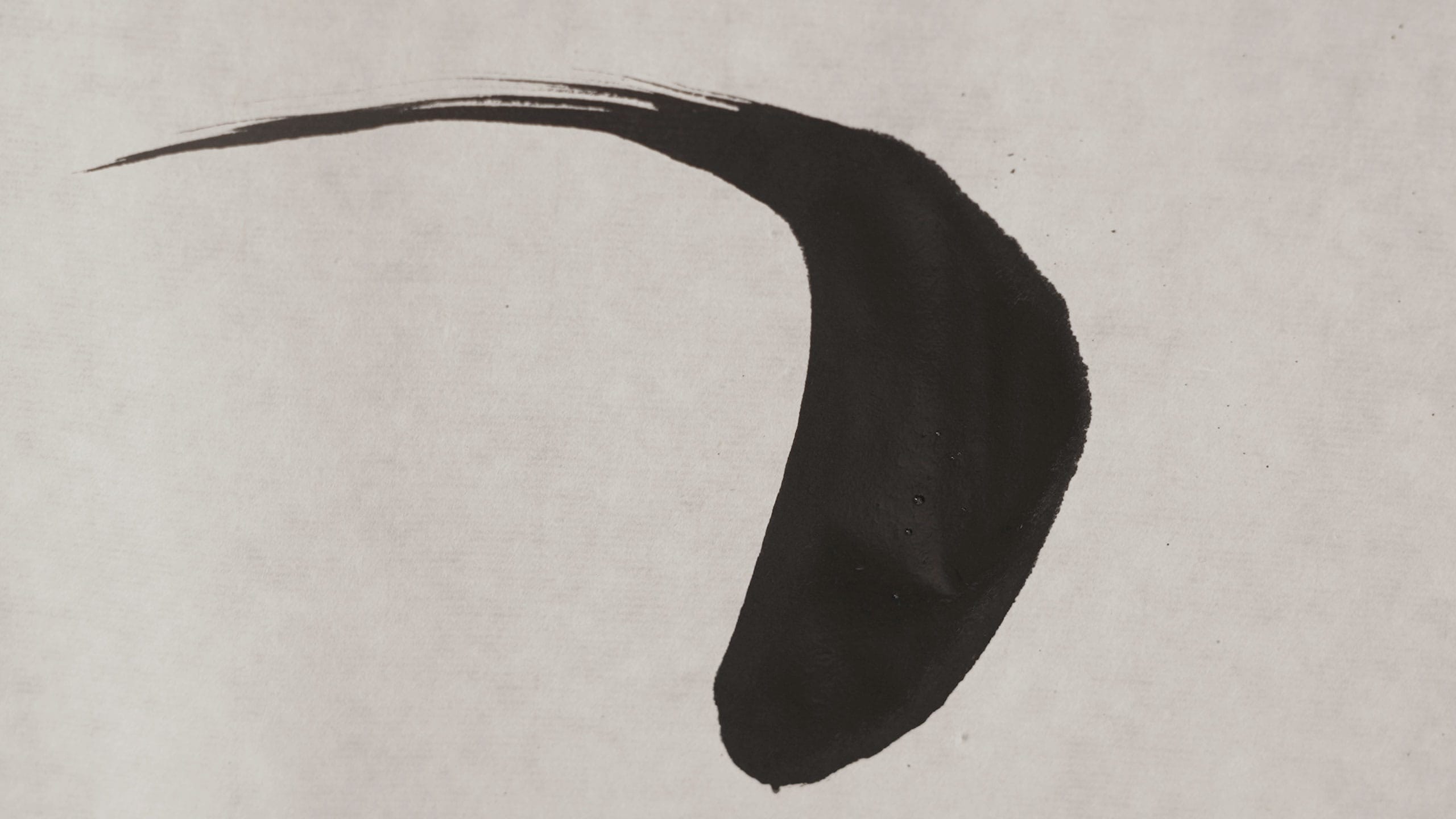A black painted brushstroke on a light grey fabric material.
