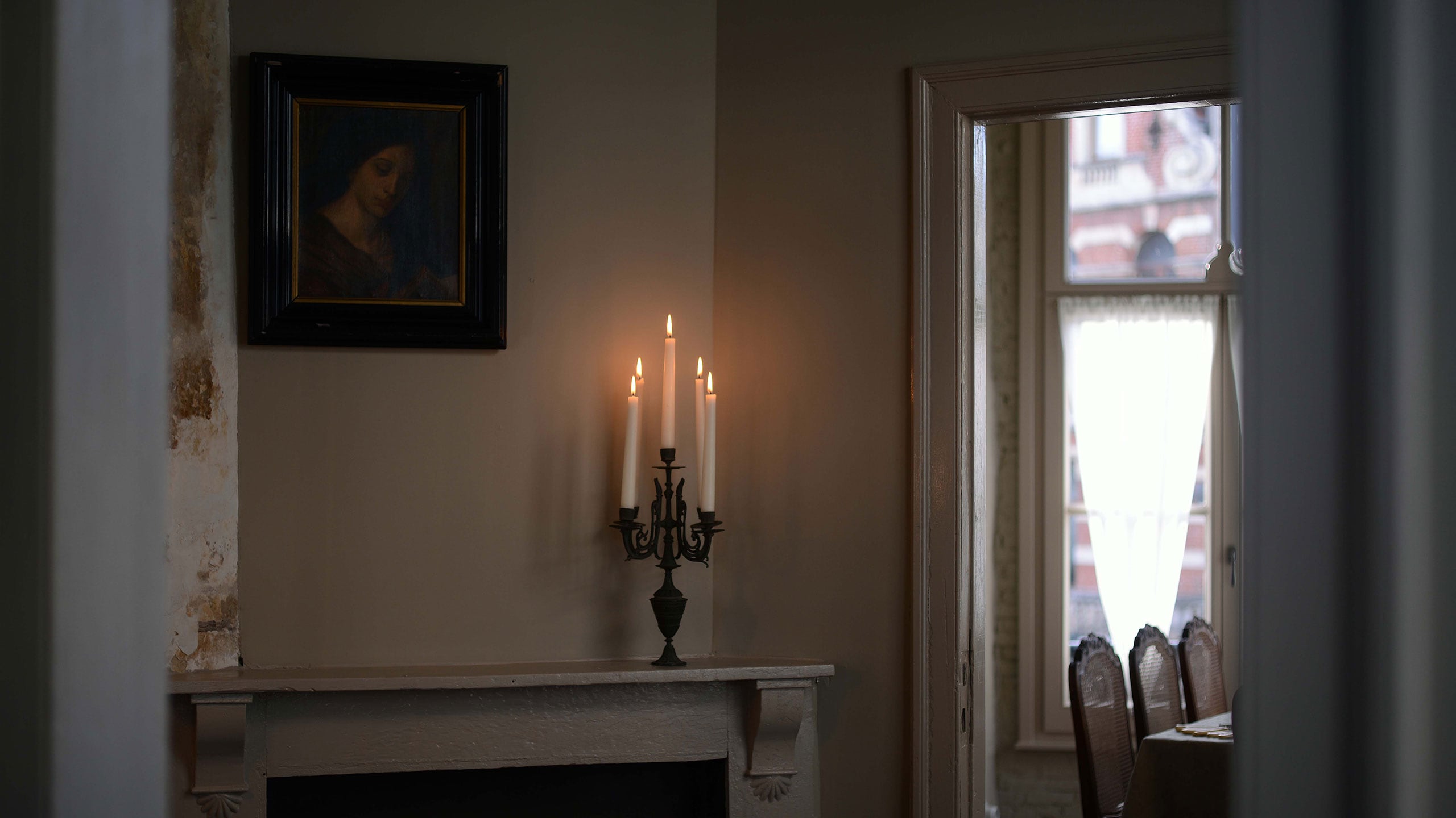 A dining room as seen from the doorway, with three lit candles in a candelabra positioned on a mantlepiece.