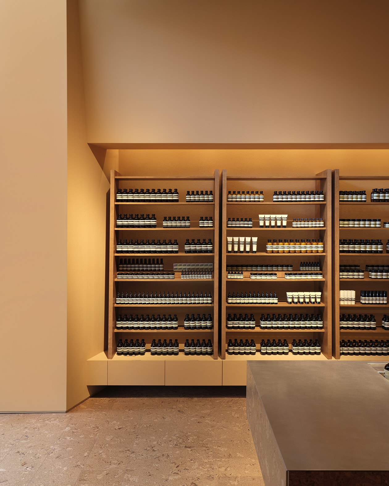 Aesop products displayed on wooden shelf in front of light brown walls