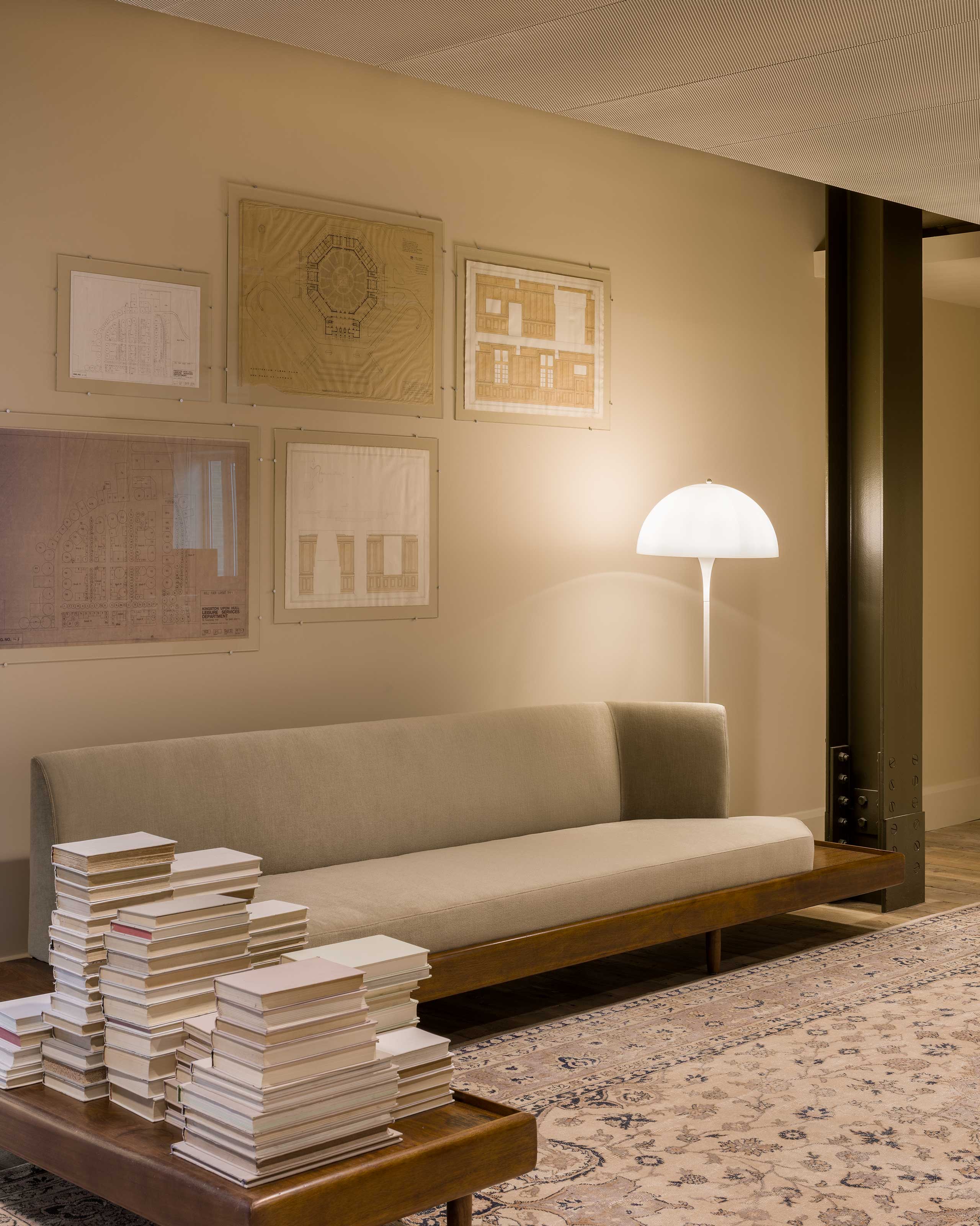 A coffee table filled with books next to a beige sofa and lamp. 
