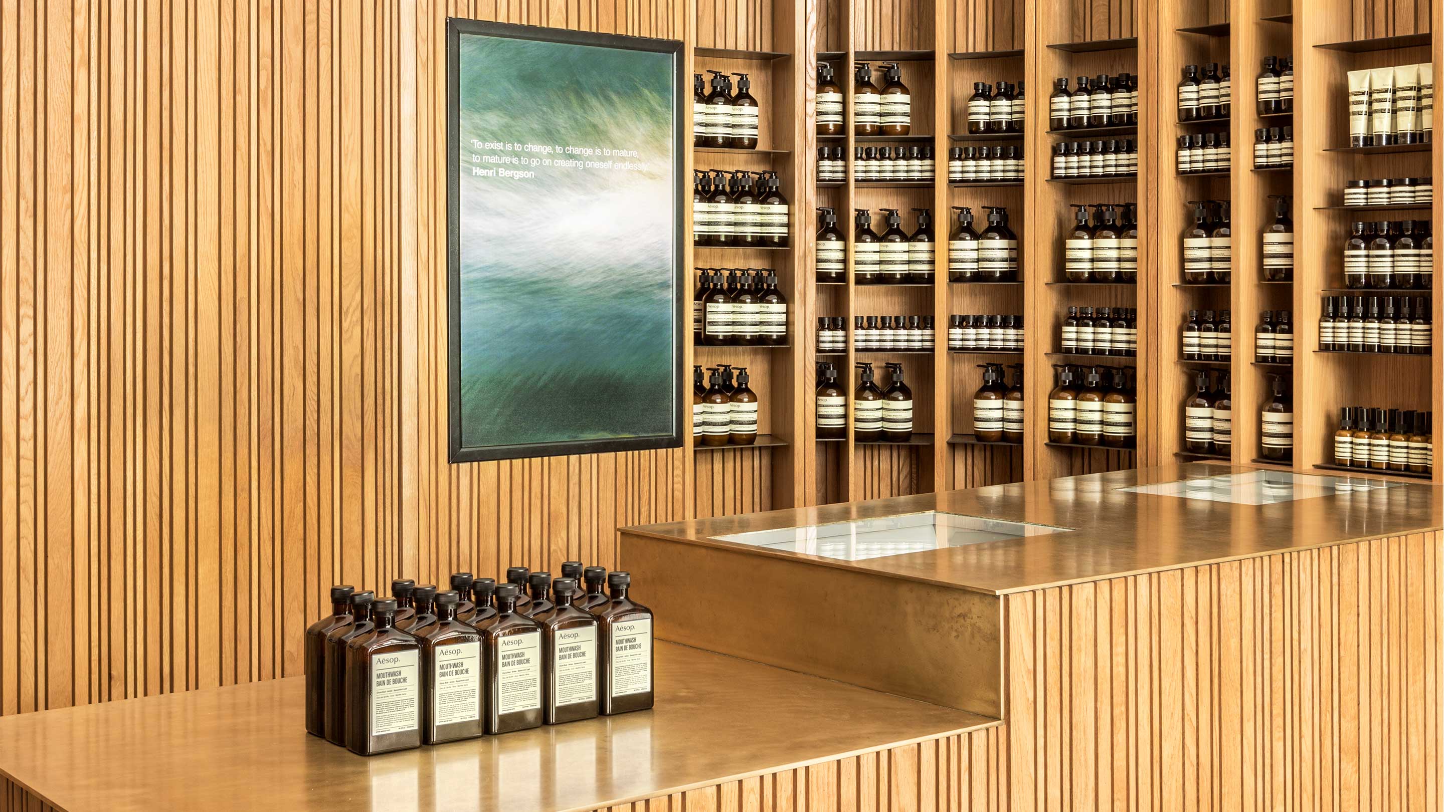 Rows of Aesop Mouthwash stored in amber bottles sit on top of a bronze counter.