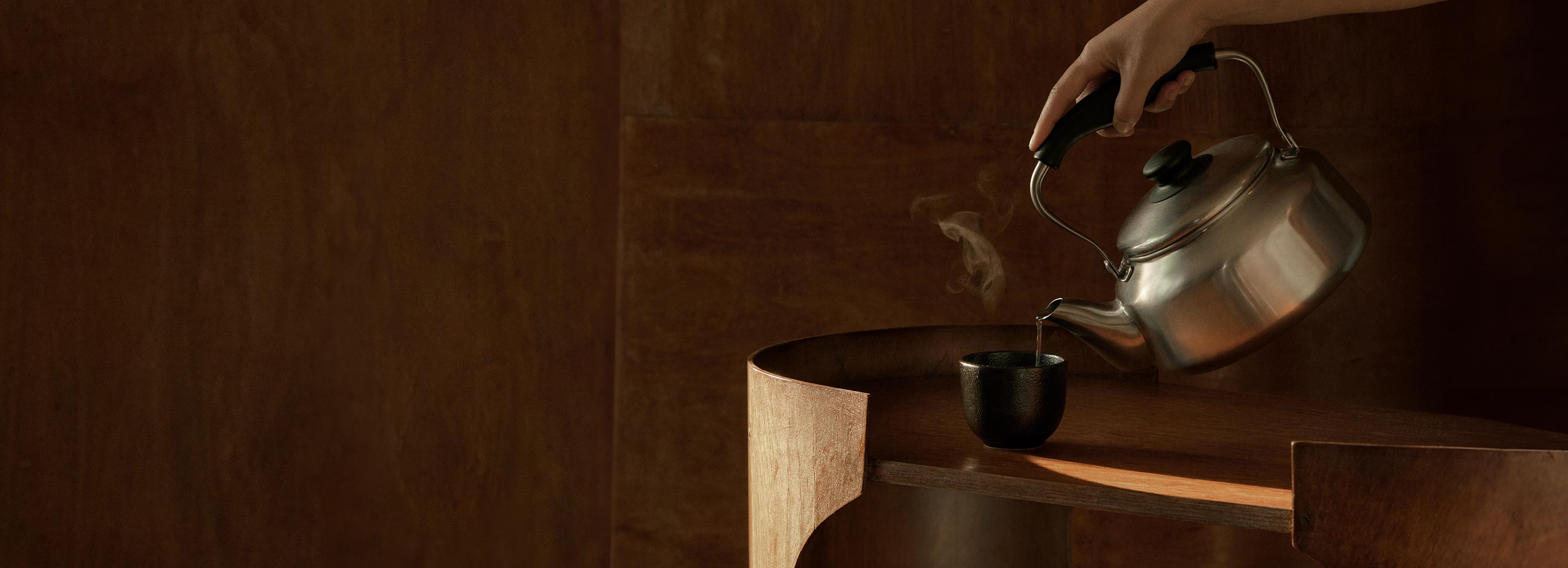 Tea being poured into a ceramic cup from a metallic kettle.