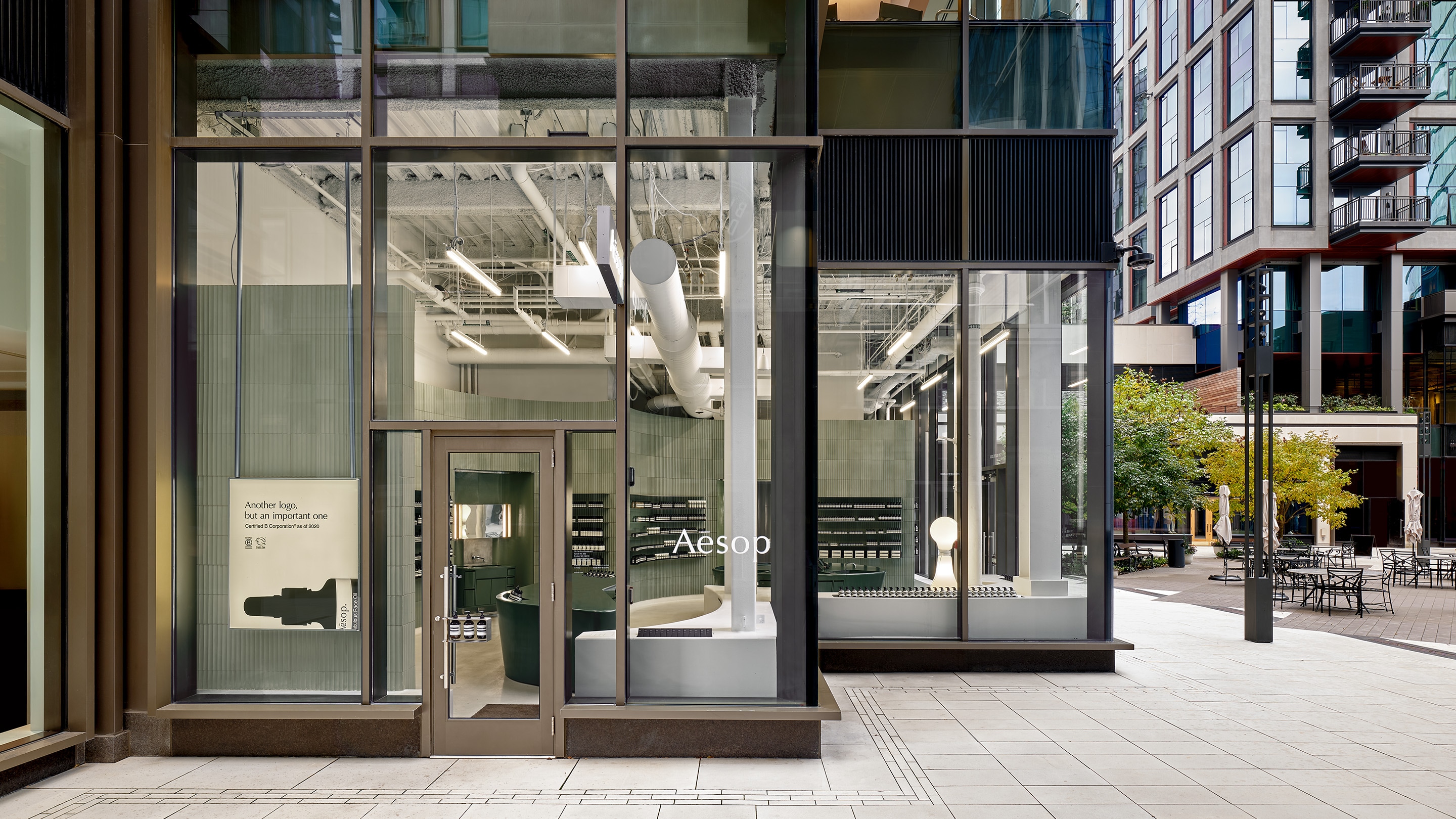 Aesop storefront featuring glass window walls on sidewalk corner with grey store interior visible through windows