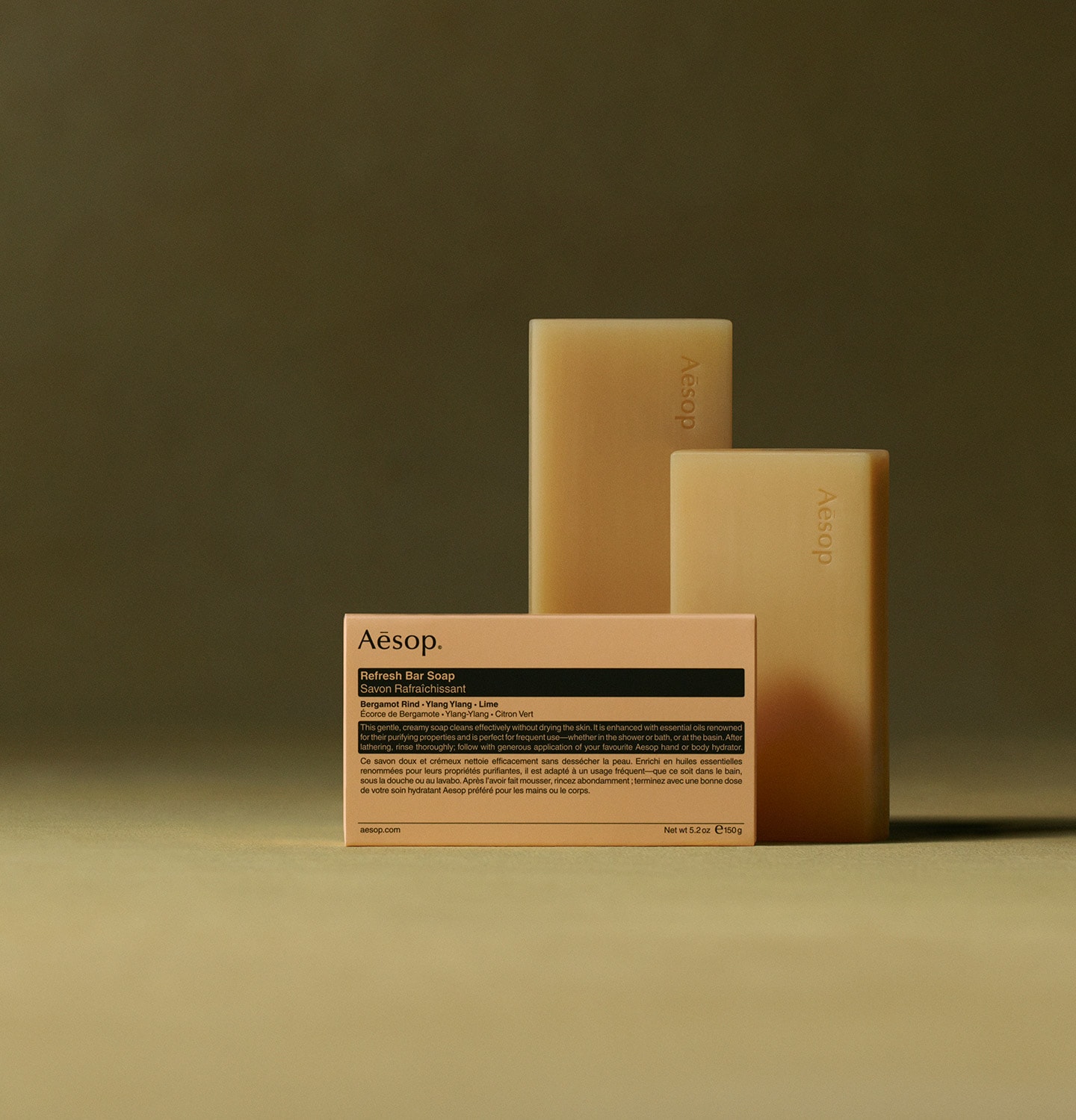 Aesop Refresh bar soaps placed horizontally behind the packaging in textured dark green background