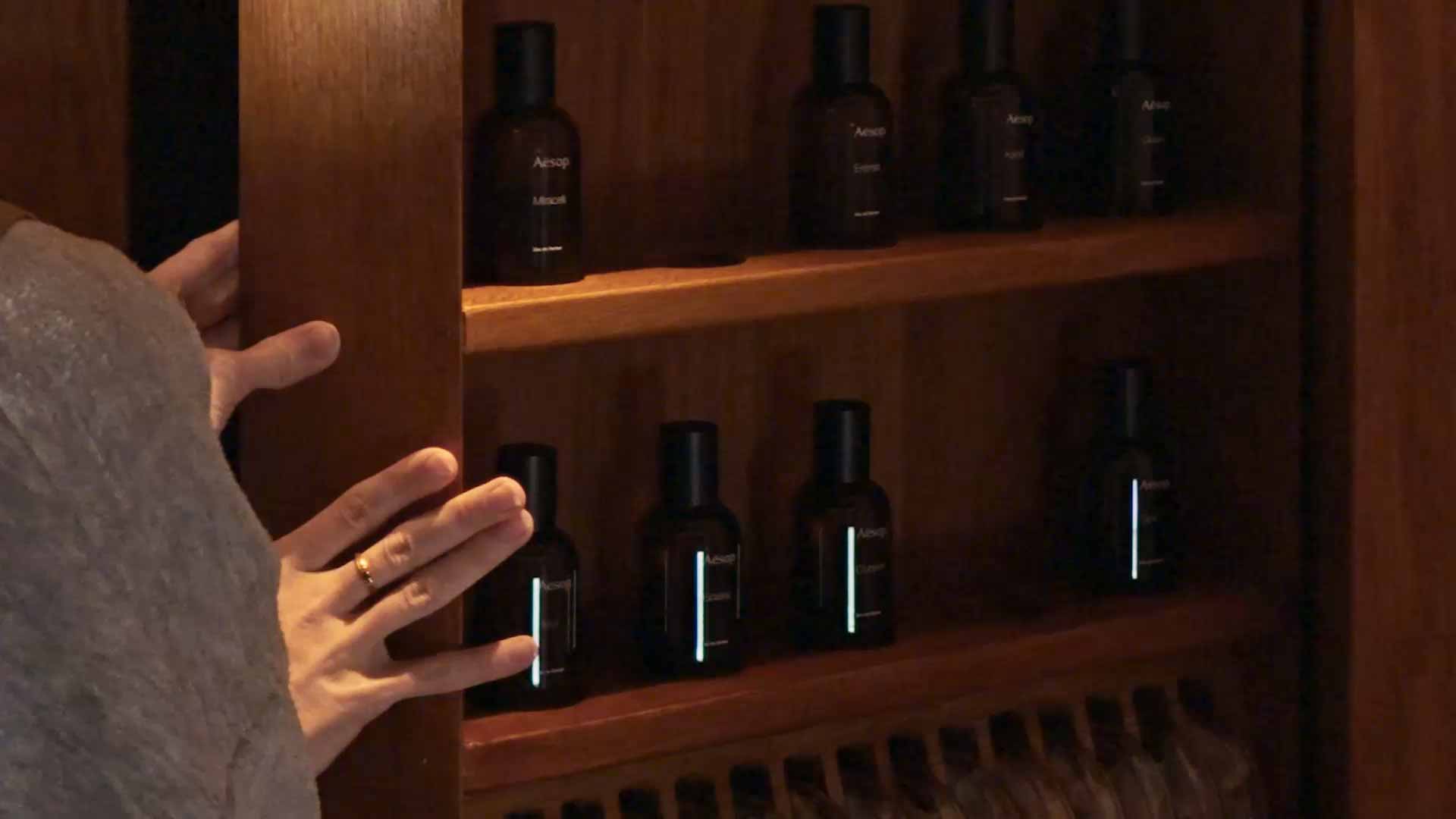 Hands holding a wooden shelve displaying Aesop fragrances