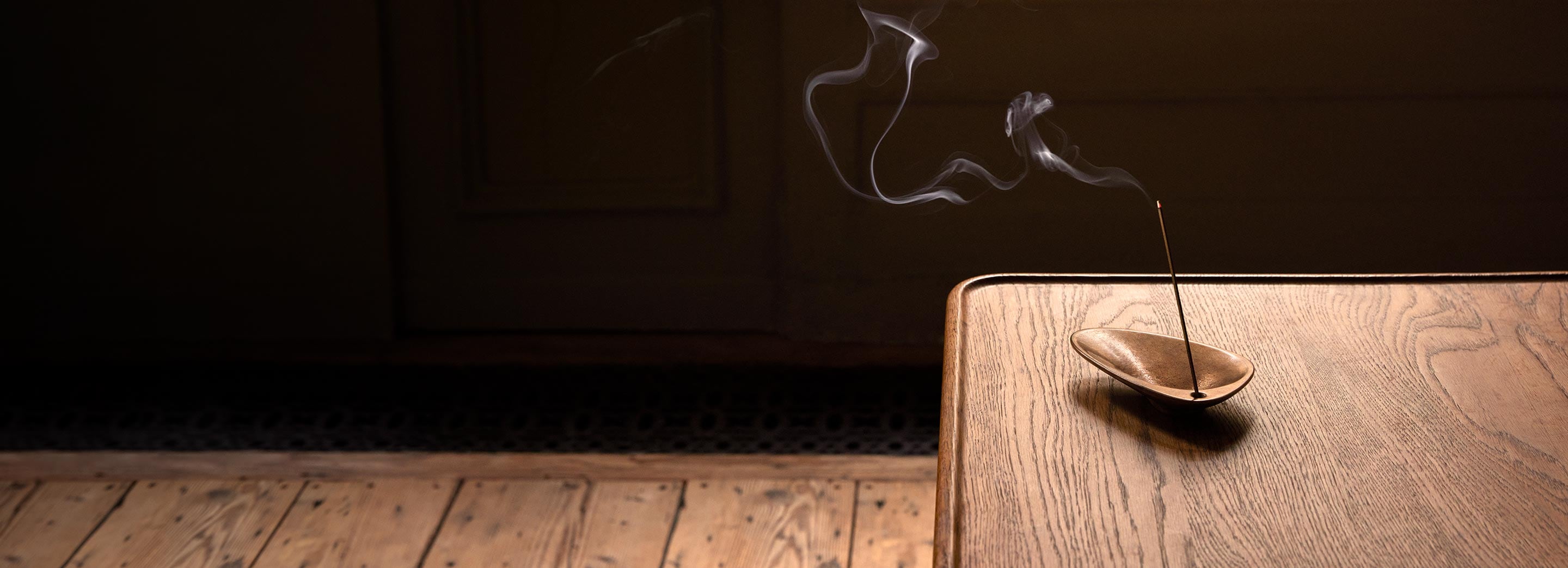 A lit stick of incense sitting alongside a mid-century chair.