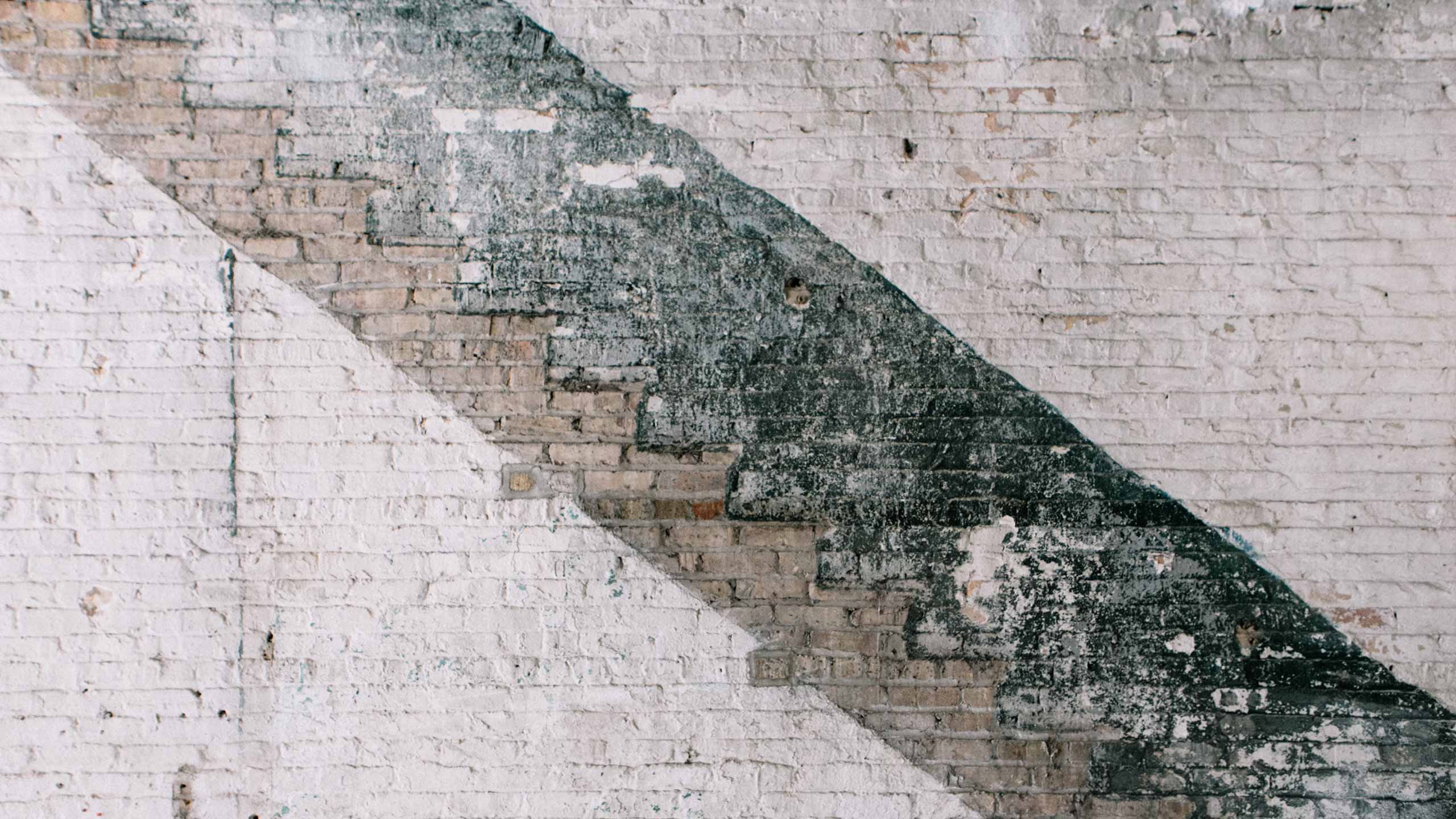 An interior exposed brick wall, painted and repainted and stripped, in shades of white and deep green.