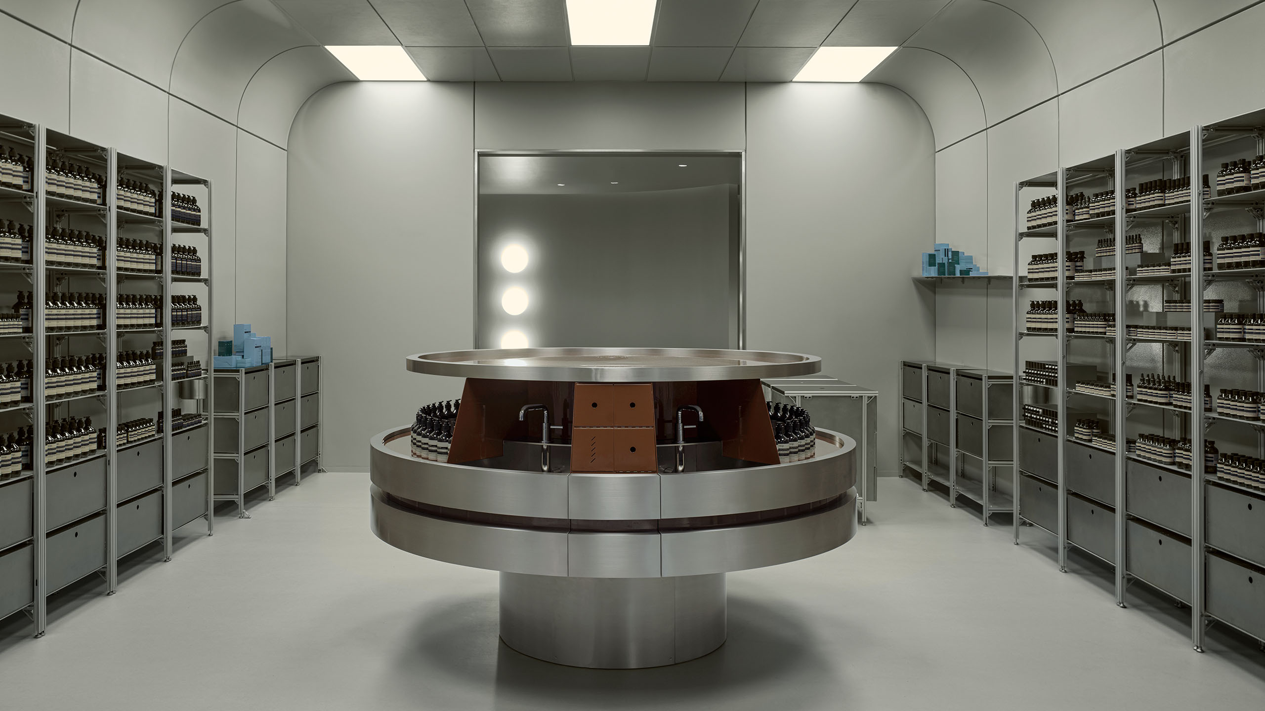 interior shot of store with grey walls, overhead lighting and paneled ceiling, steel shelving with products lining the walls, and a large circular basin in the center of the room