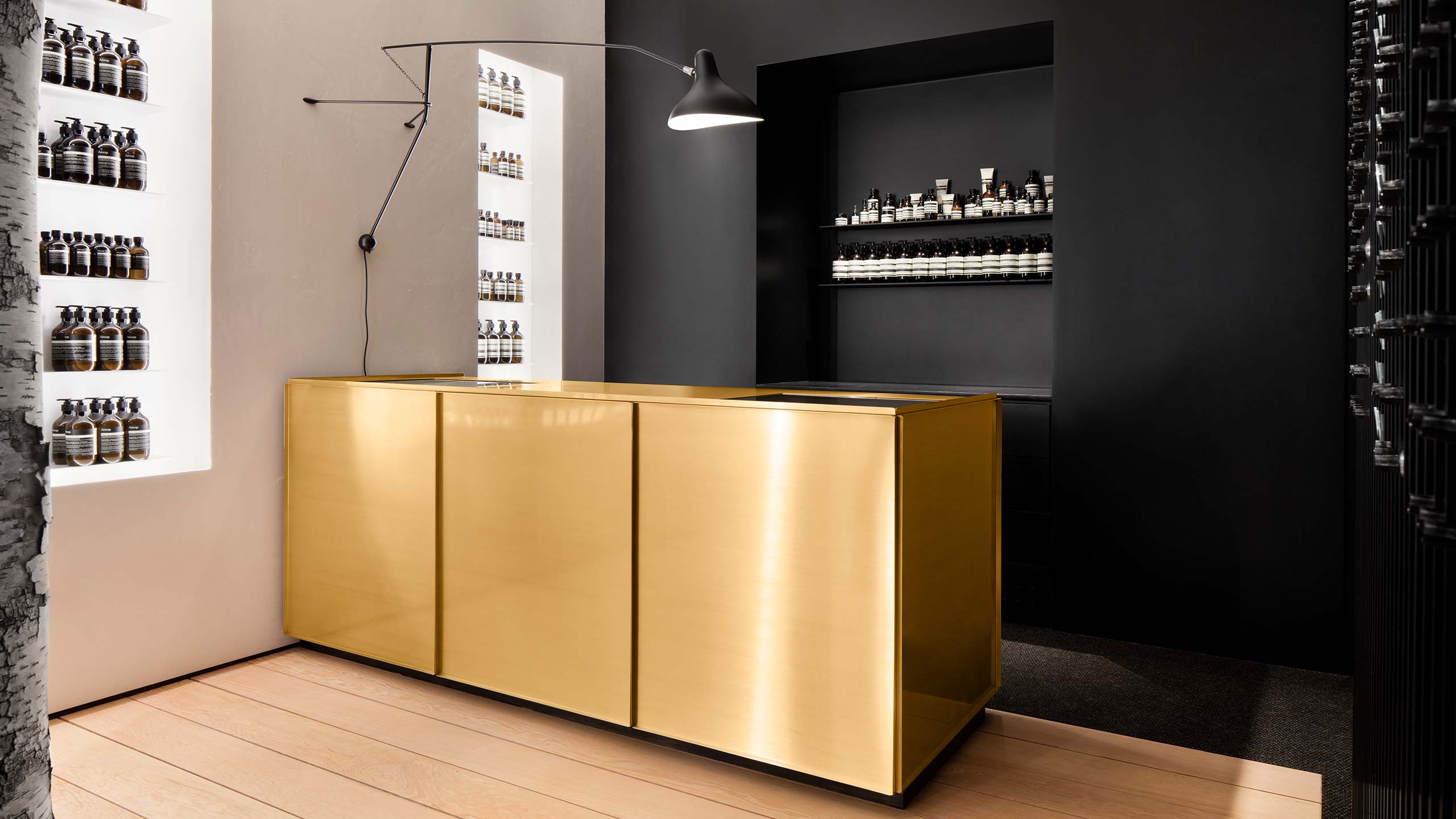 A brass counter top contrasting with a black wall holding Aesop product