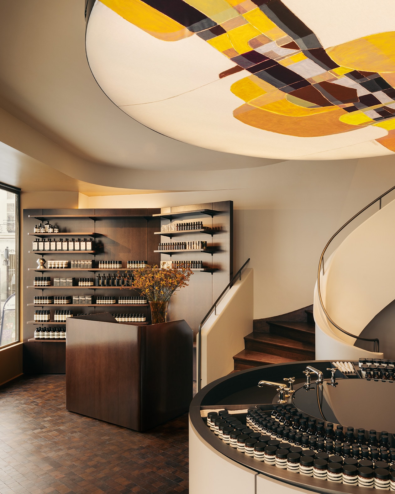 Aesop Rue de Sèvres store interior displaying ceiling light, metal basin and wooden product display stands.