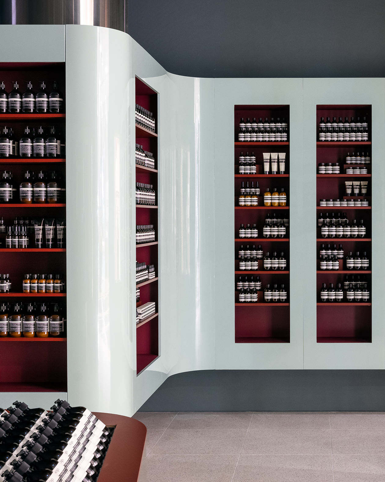 Several rows of red shelves in light blue walls displaying Aesop products.