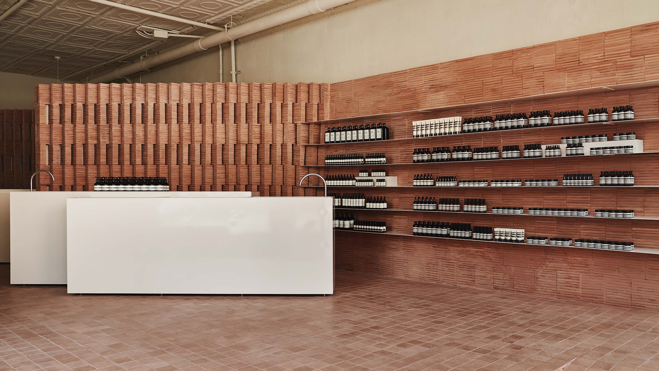 Aesop Park Slope store interior, with large white counters placed in front of tessellated brick wall