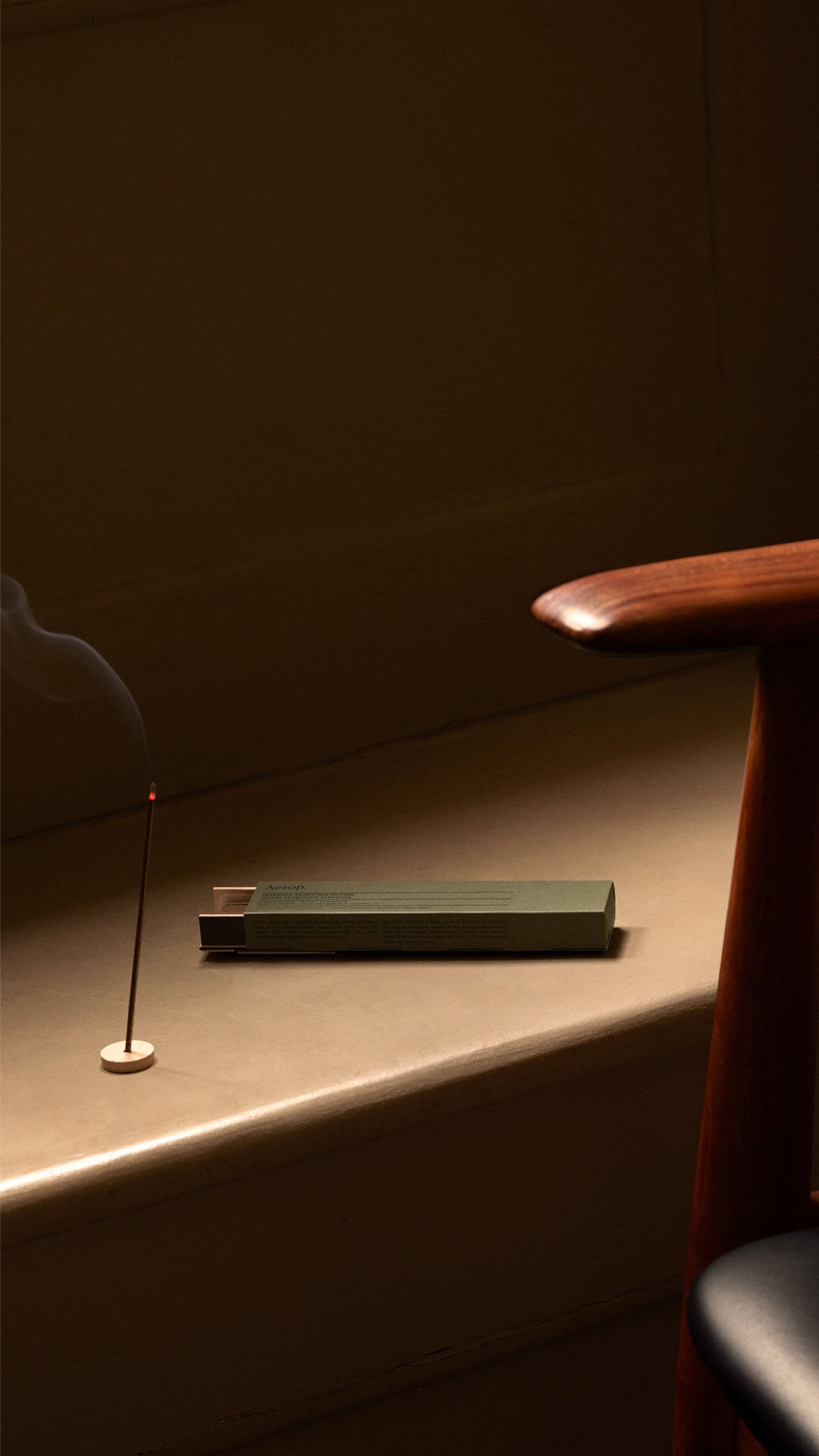 A lit stick of incense sitting alongside a mid-century chair.