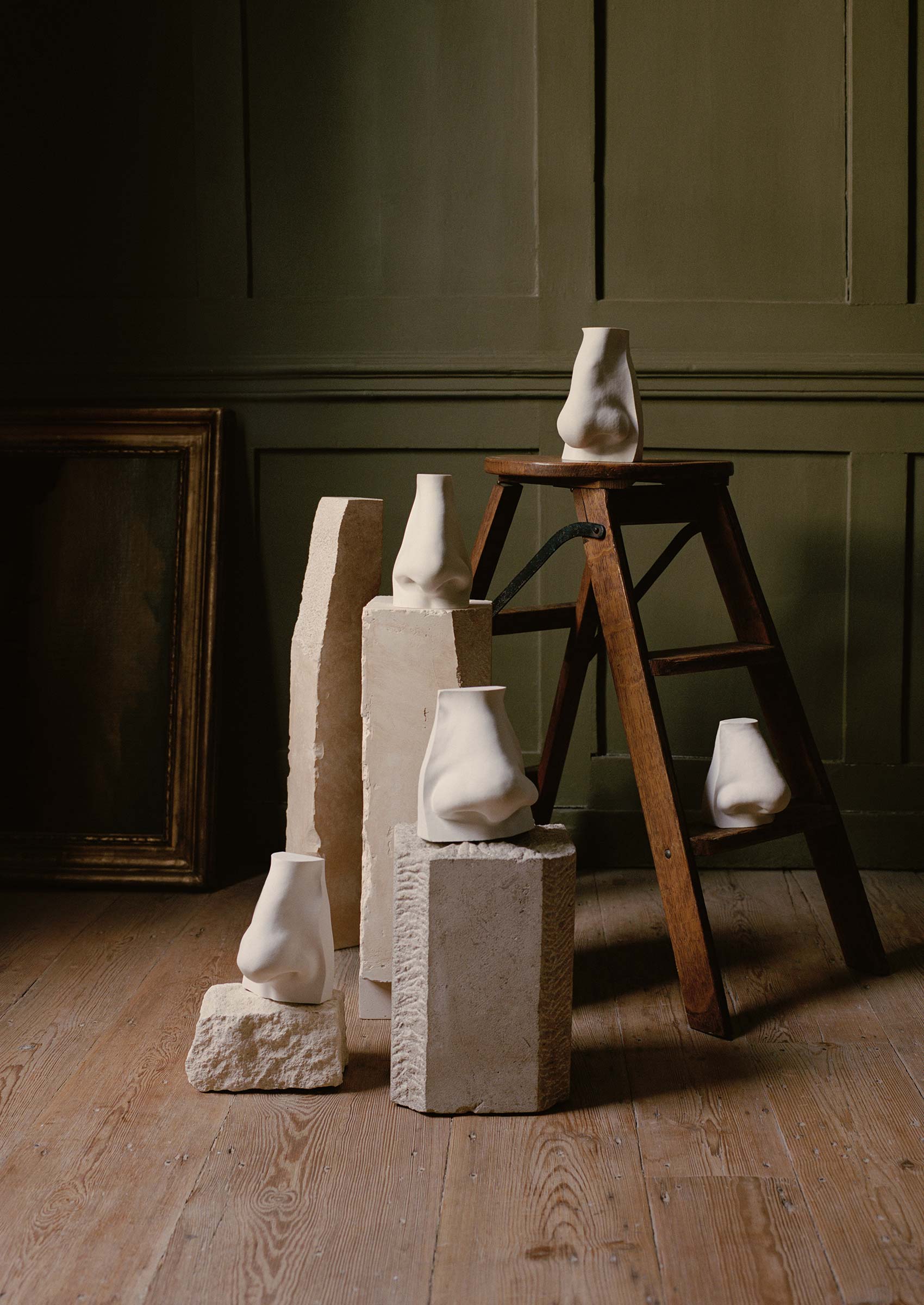 Plaster sculptures of noses resting on stone podiums and a wooden ladder.