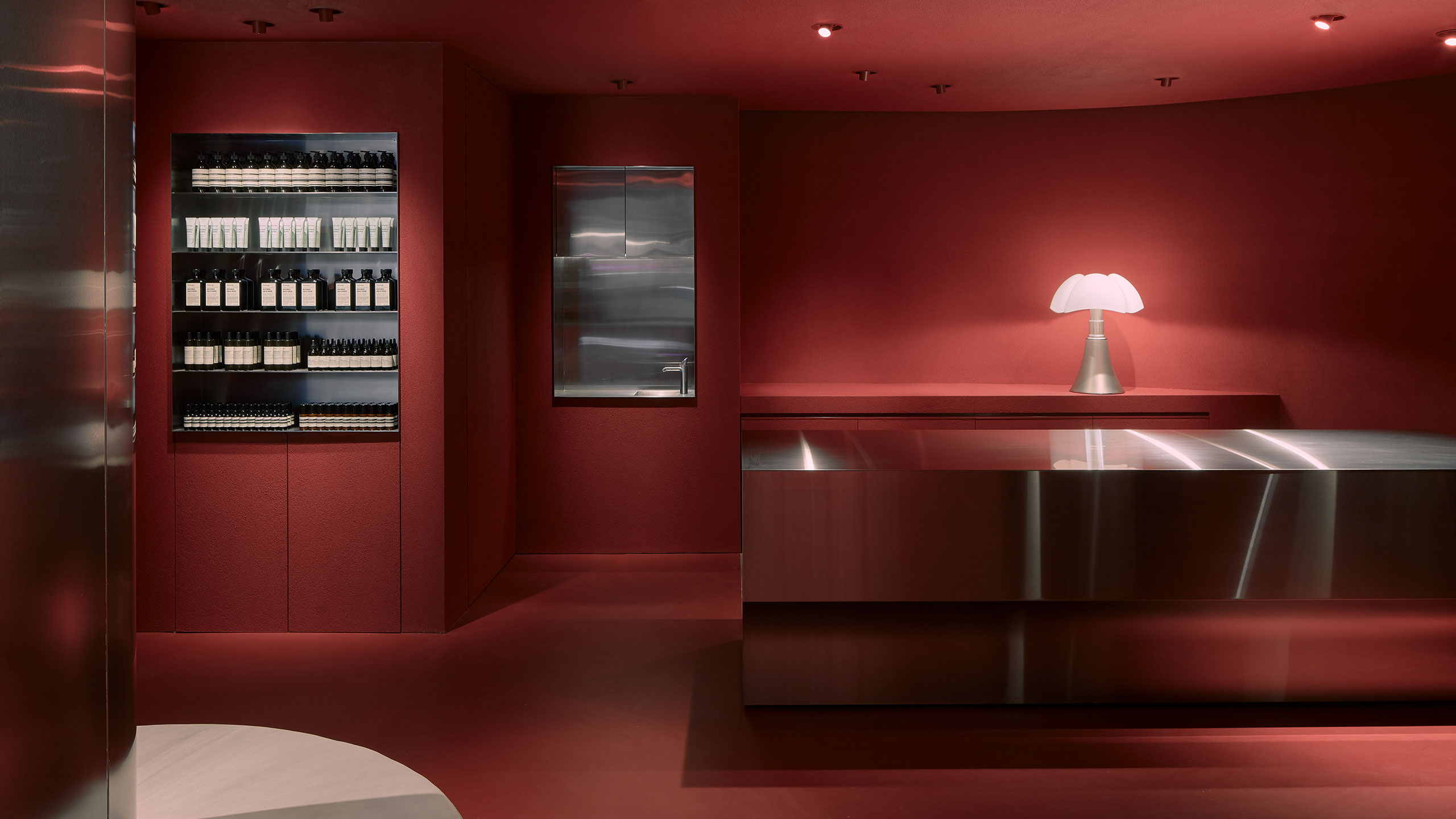 Dark red walls flank a brushed stainless steel counter. There is a bright mushroom lamp on a red counter-top in the background.