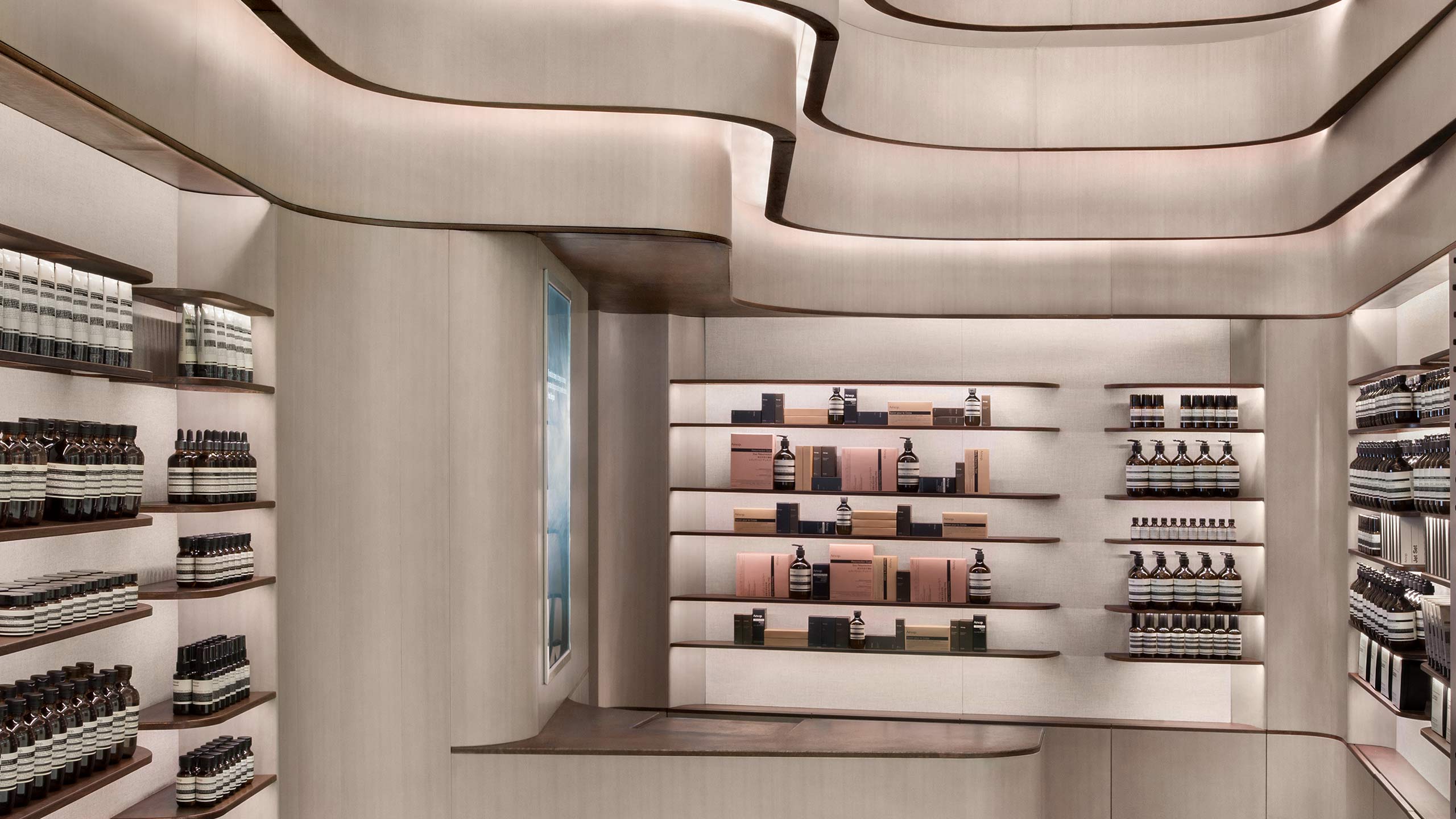 Curved lines and LED lines span across the walls around shelves holding Aesop product. 