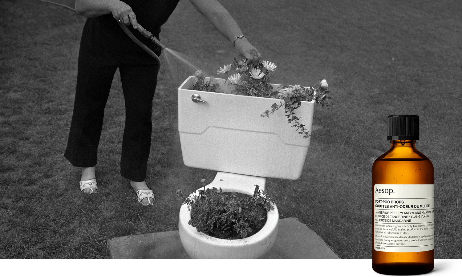 Retro black and white photograph depicting a woman outdoors using a hose to water flowers growing out of a toilet bowl.