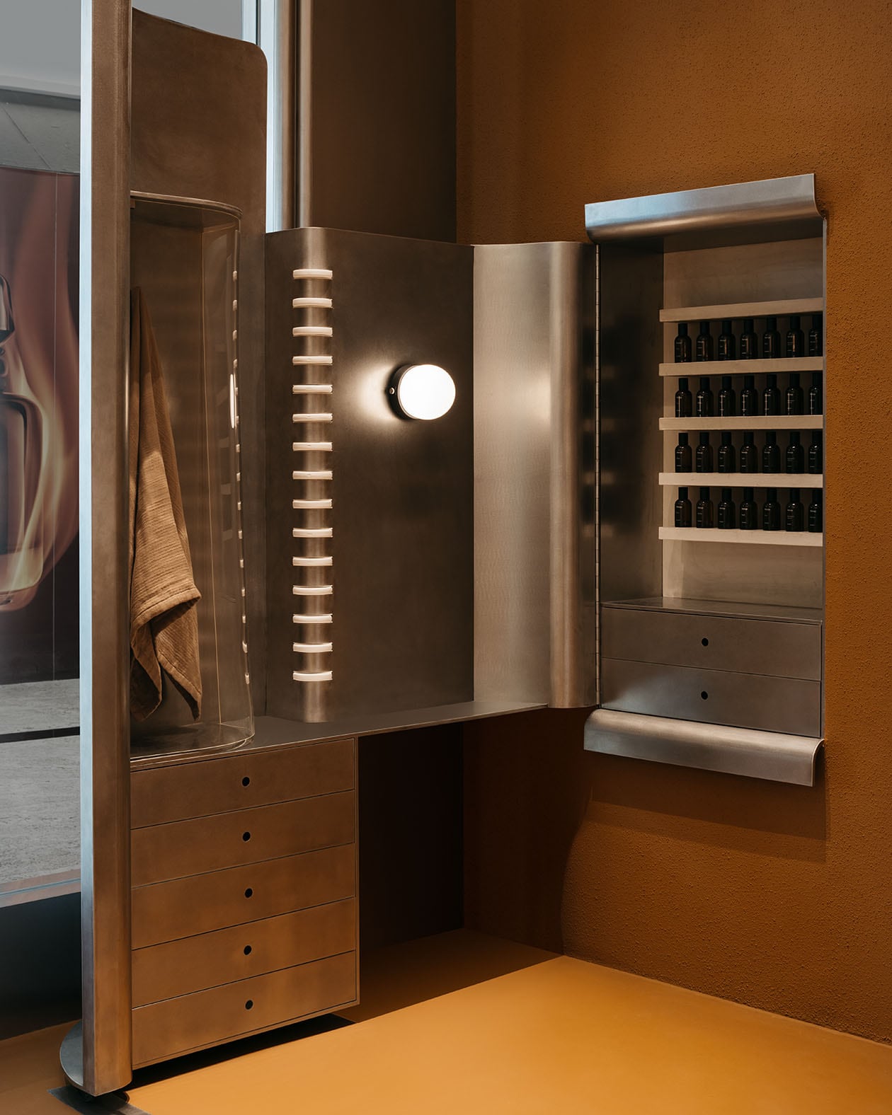The polished metal tables as the reflective phone booths are reimagined as a Fragrance Armoire.