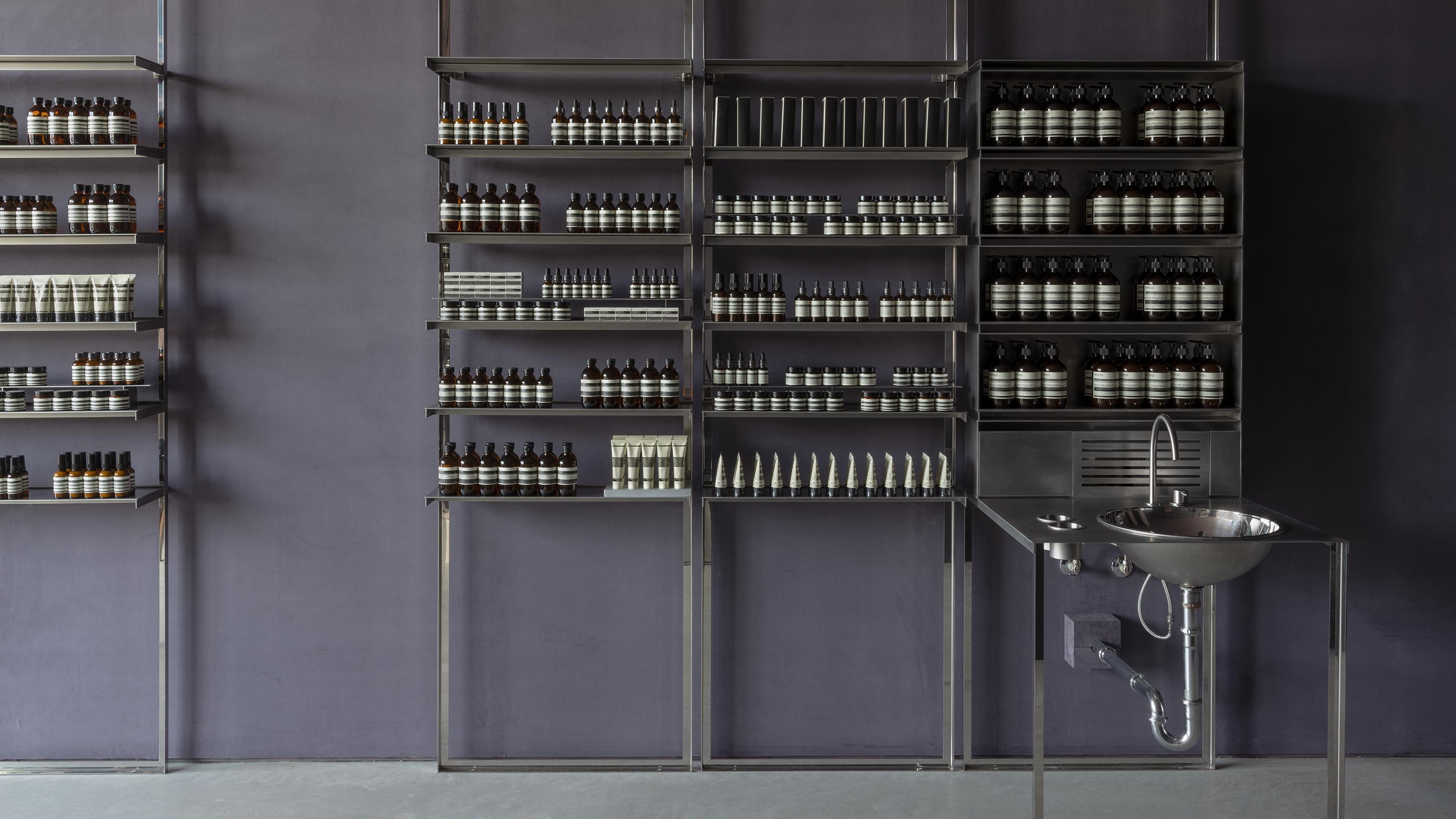 Contemporary steel shelves holding a range of Aesop product next to an industrial chrome sink.