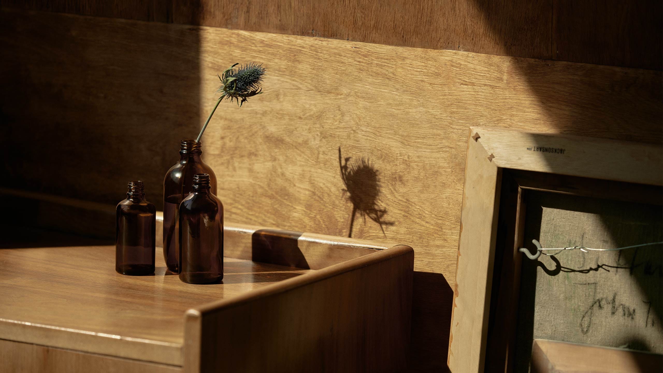 Brown bottles sit on a wooden platform with sunlight reflecting their shadows.