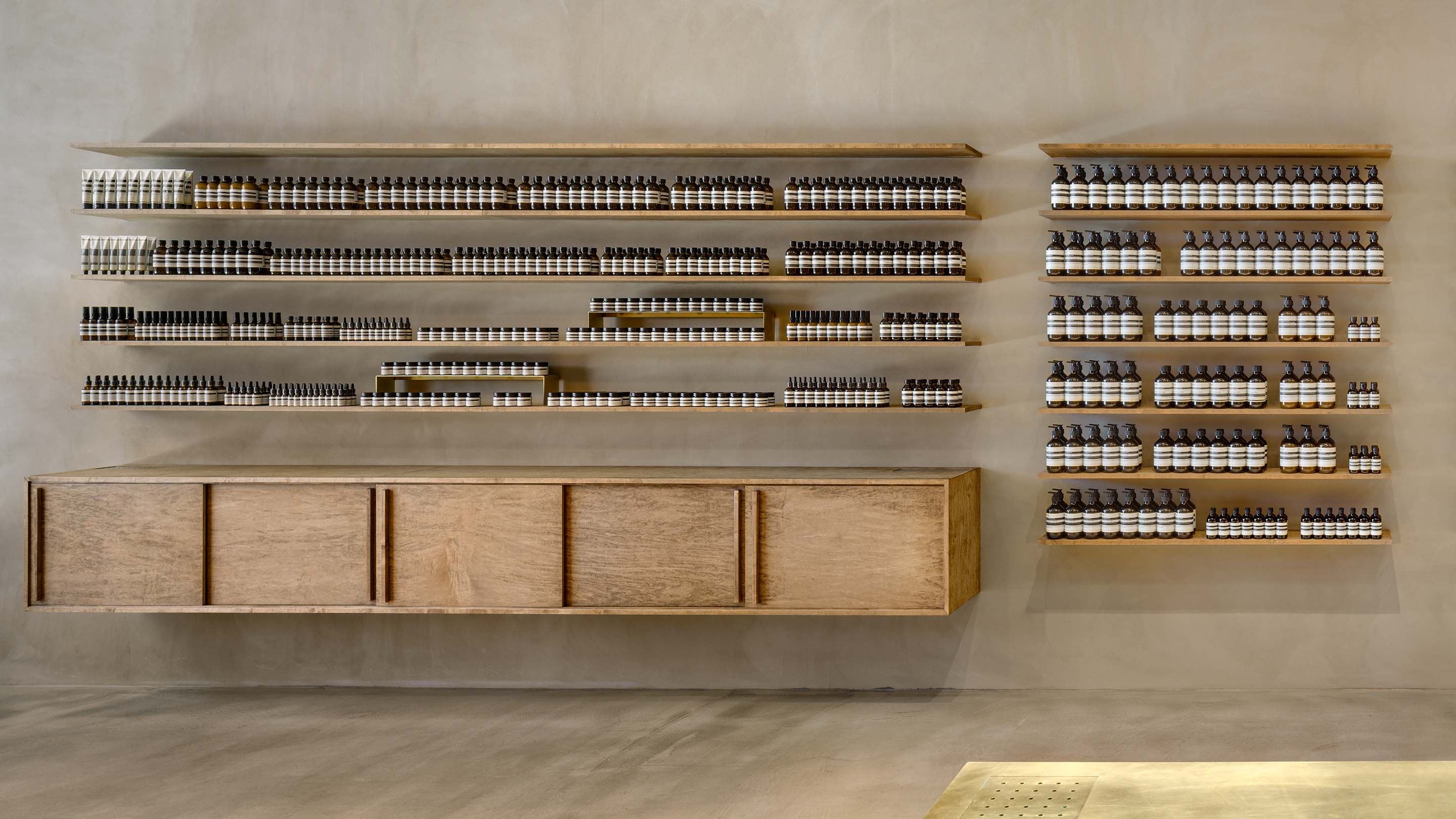 A beige wall featuring maple wooden floating shelves holding Aesop product.