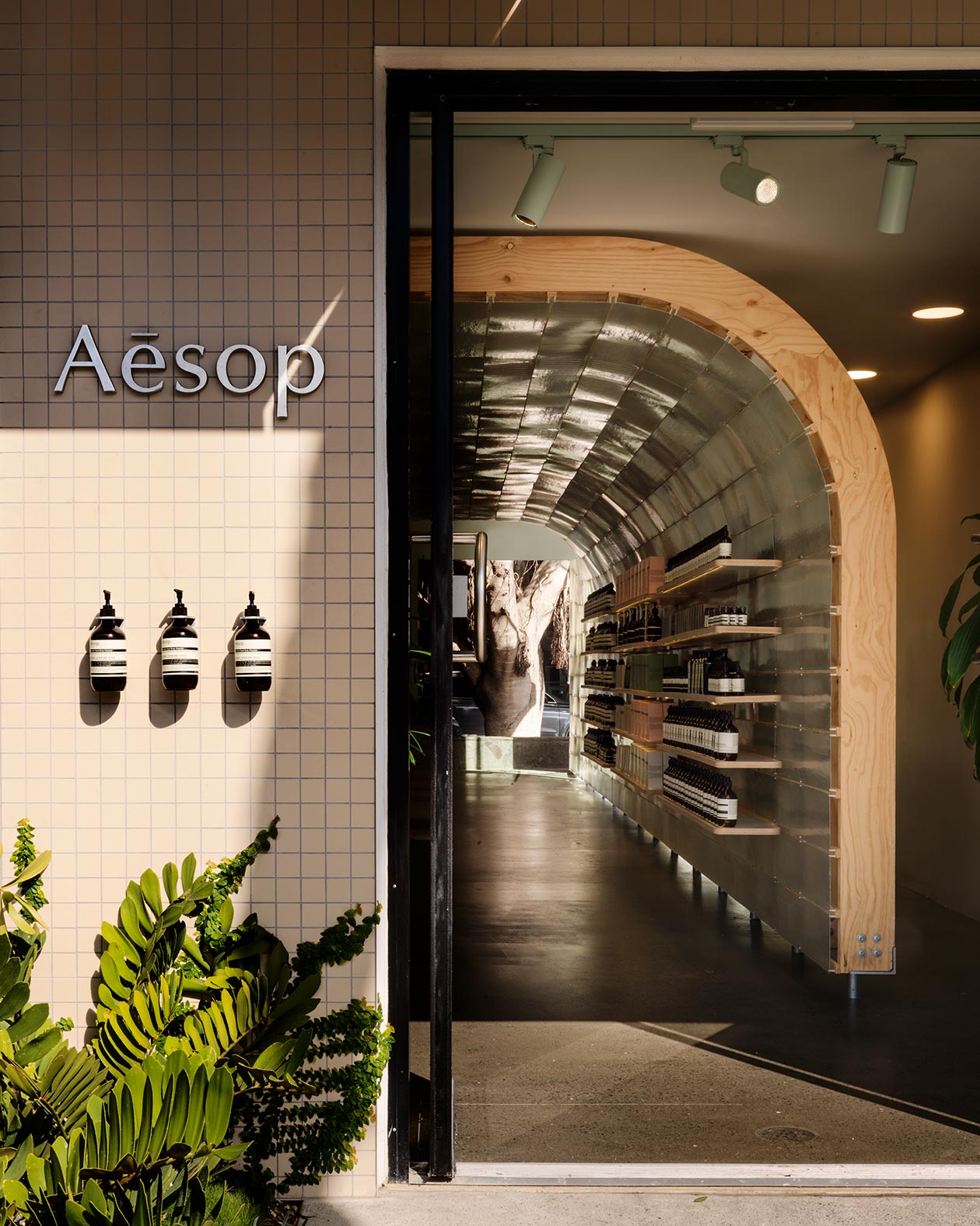 The entrance of Aesop James Street showing the tiled exterior. Three bottles of Aesop product hang by the entrance.