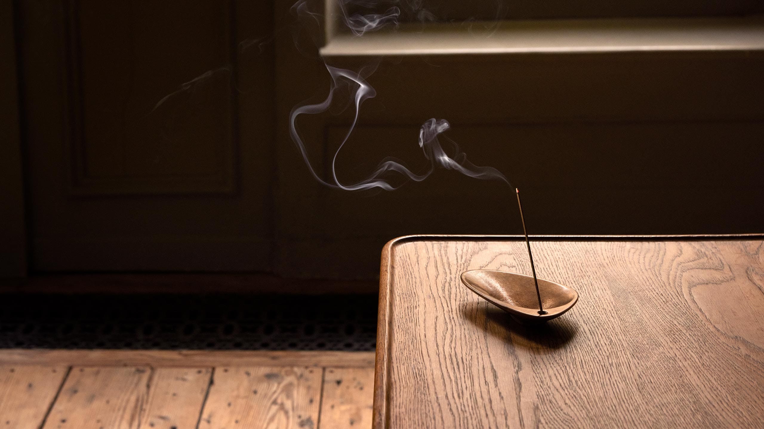 A lit incense stick resting in the Bronze Incense Holder on a wooden table.