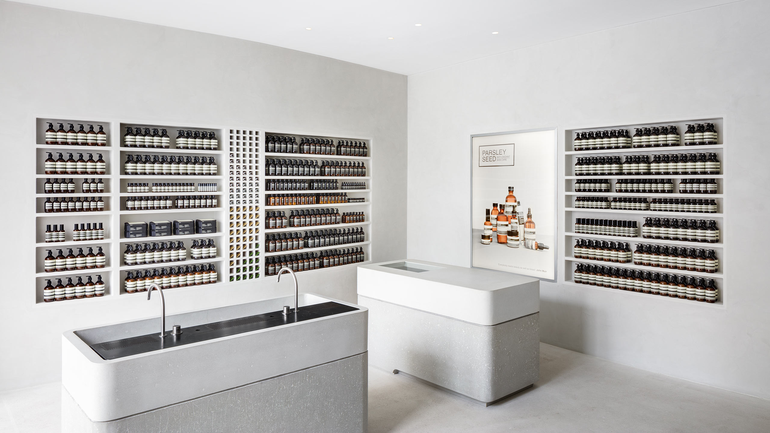 Store interior featuring shelves of Aesop product; curved-edged sinks sit in an off-white painted space.