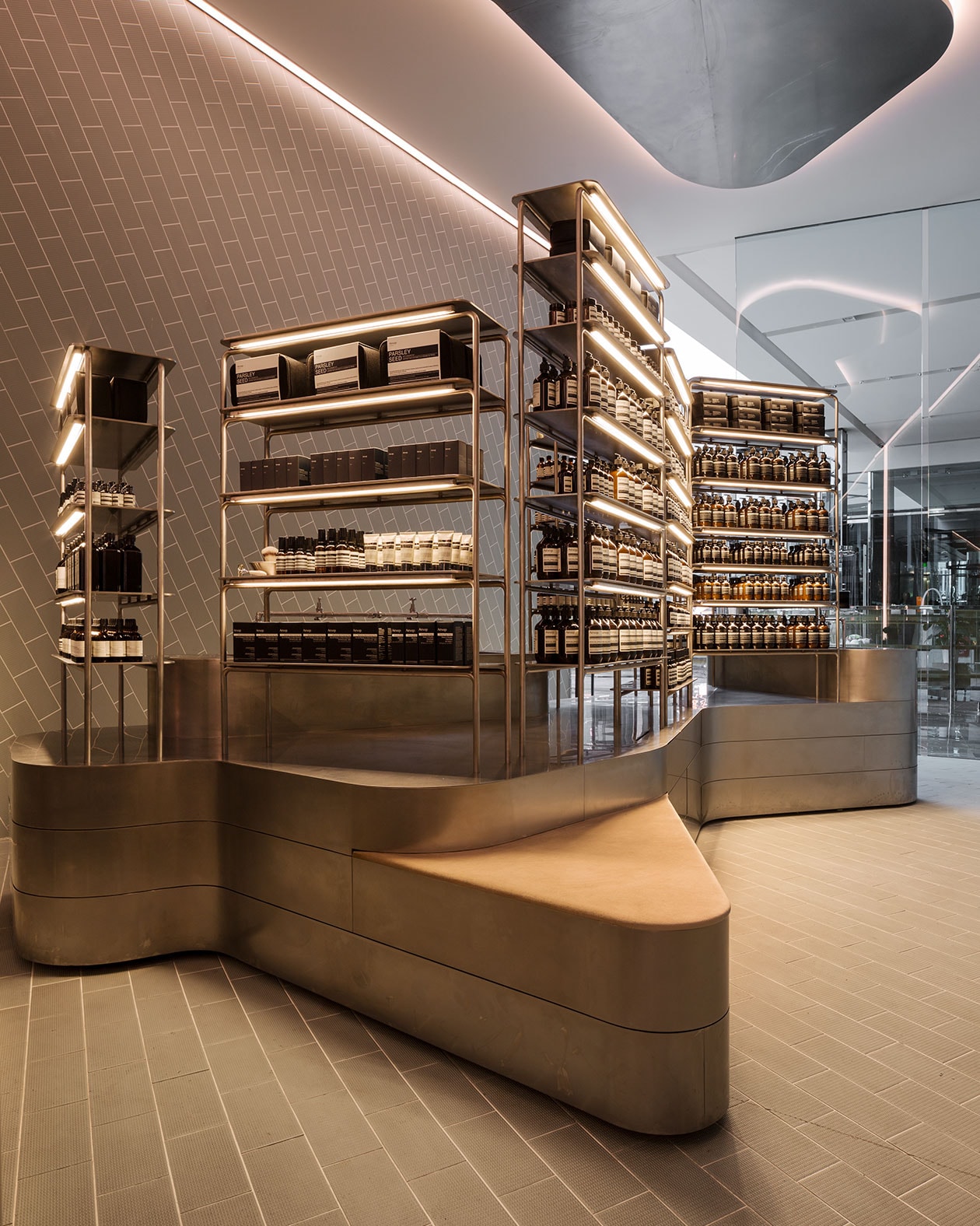 Brushed steel bench seating surrounded by steel pipe shelving. The walls feature porcelain and edged, tube lighting. 