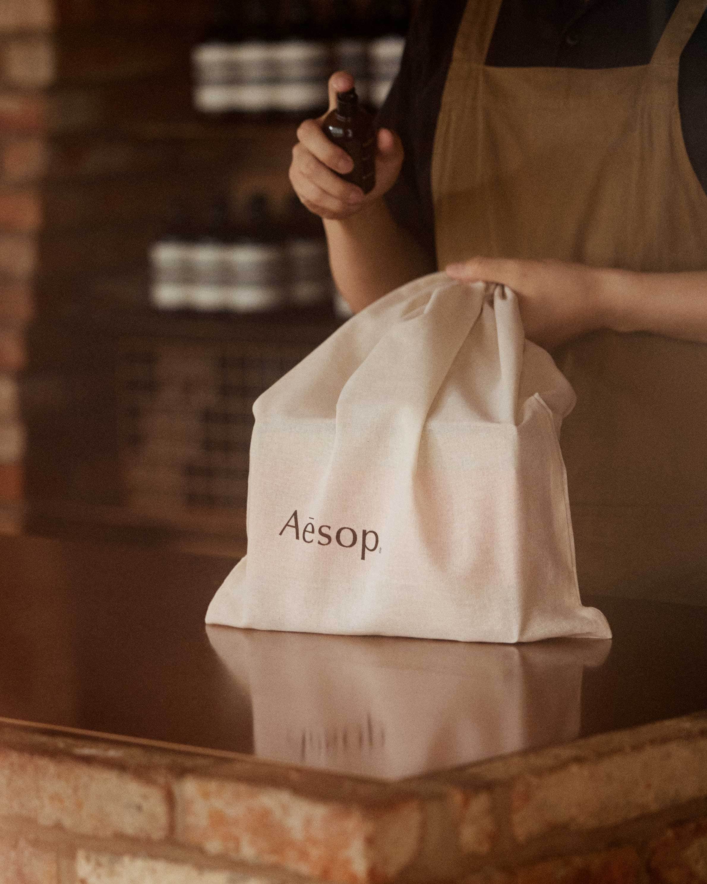 Aesop consultant spraying Aesop fragrance on a cotton bag