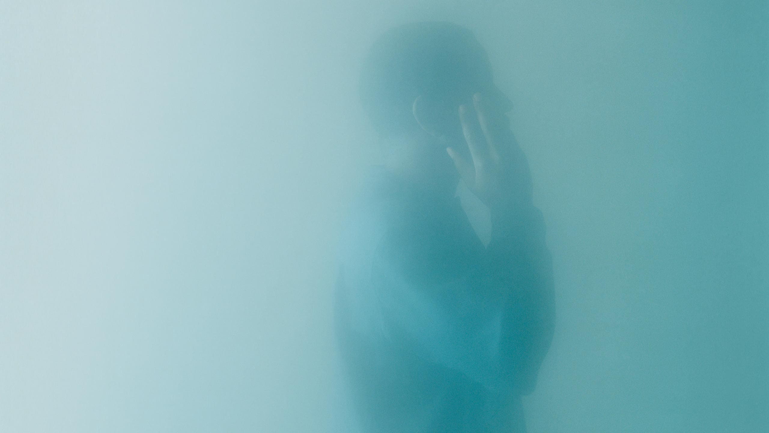 The profile of a figure applying serum to their face, obscured in a cyan haze.