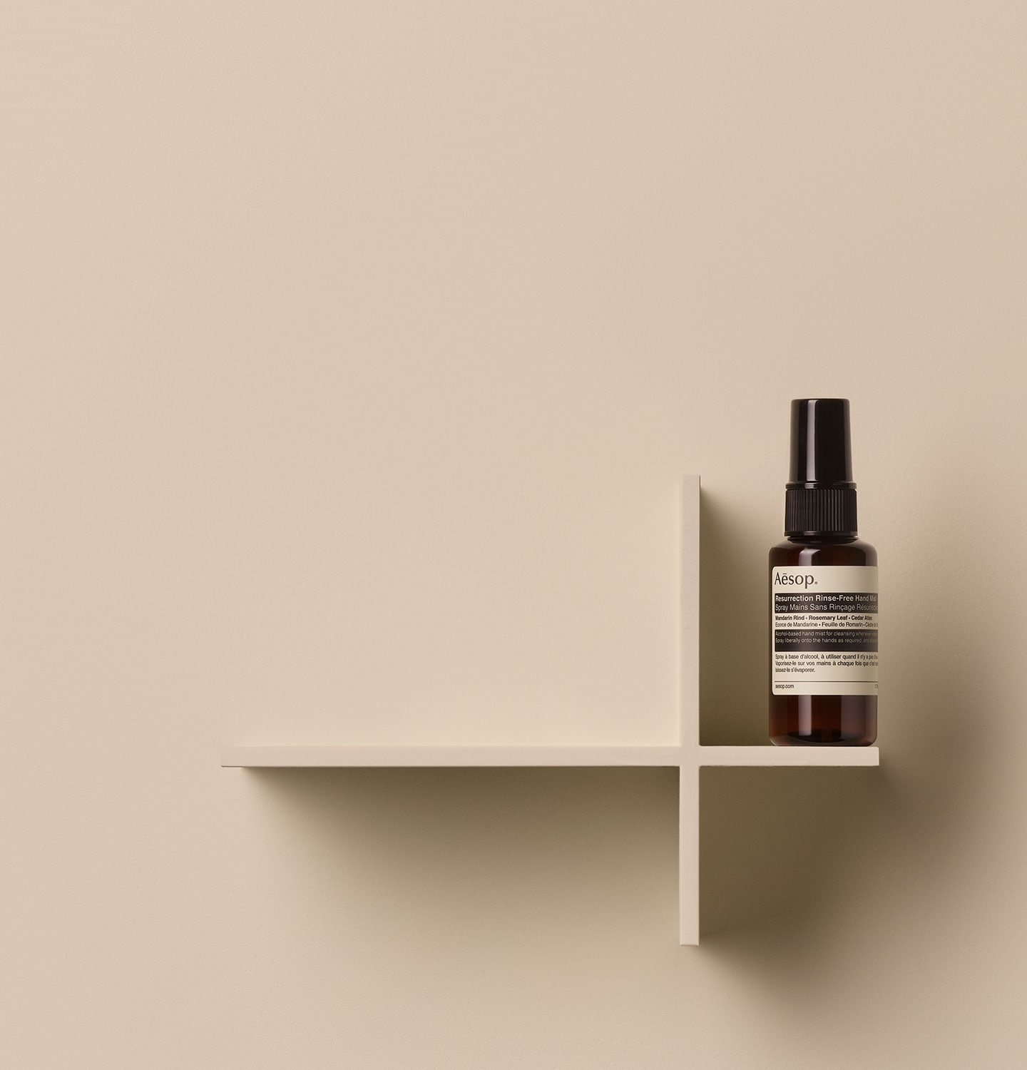 Aesop Resurrection Rinse-Free Hand Mist in small amber spray bottle arranged on a wooden object in a beige background
