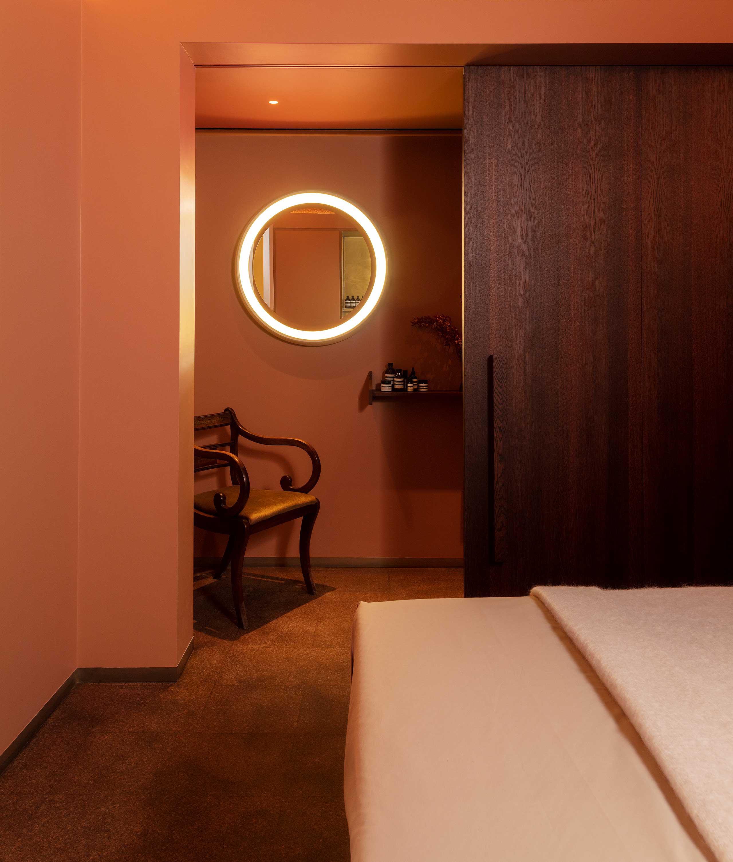 Aesop facial treatment room interior with massage bed next to a window, and white wooden walls