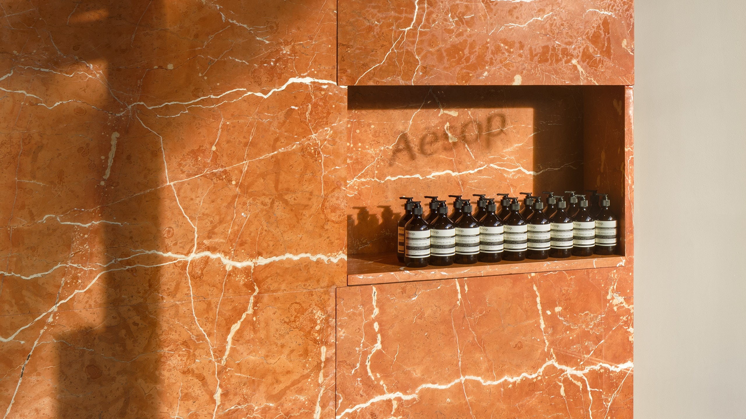 Aesop Greenwich Connecticut Store Interior, featuring products stacked within a wall recess below the shadow of the Aesop logo.